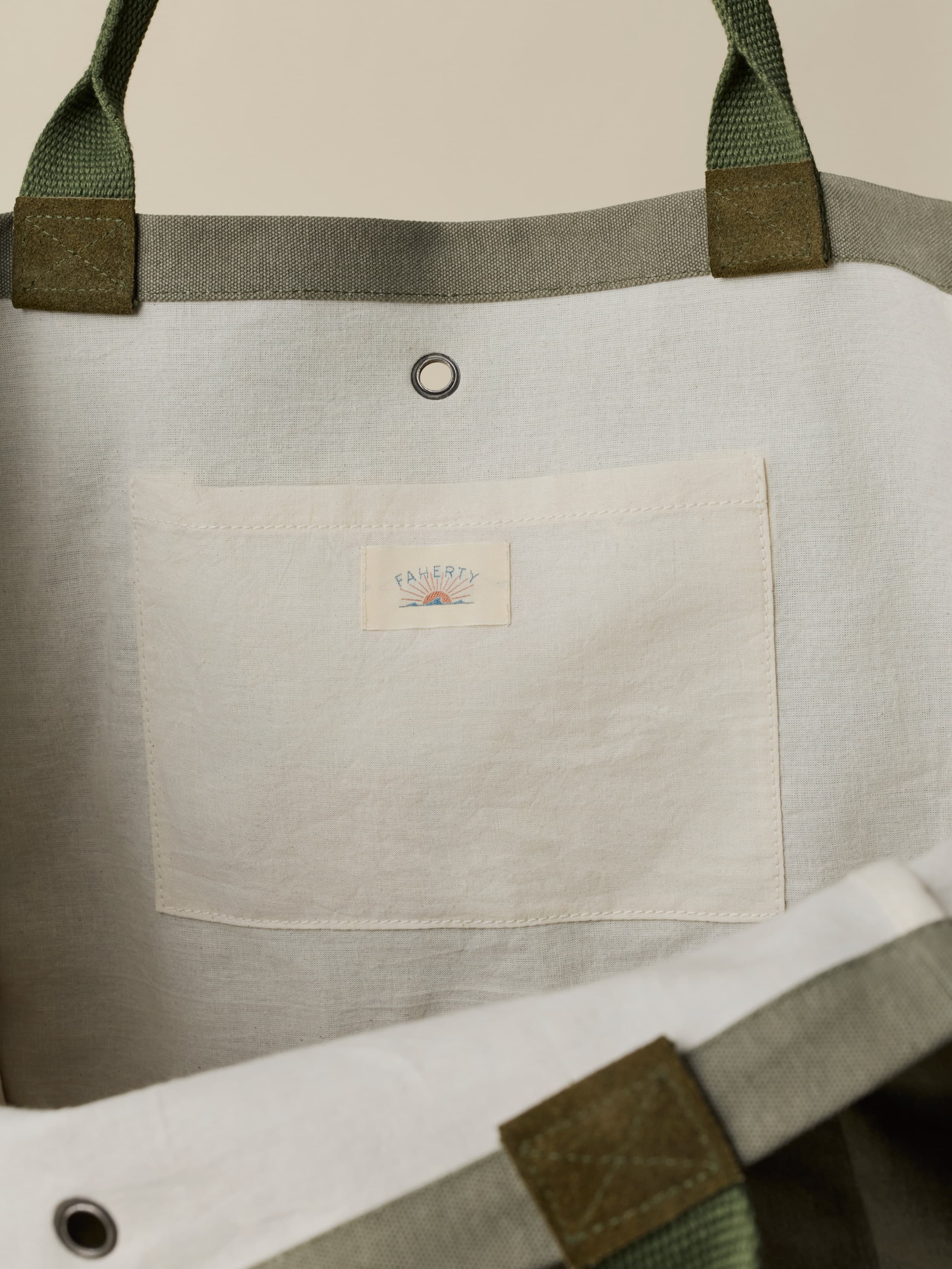 Close-up of the inside of a green tote bag with green straps and a visible Faherty brand label on a beige background