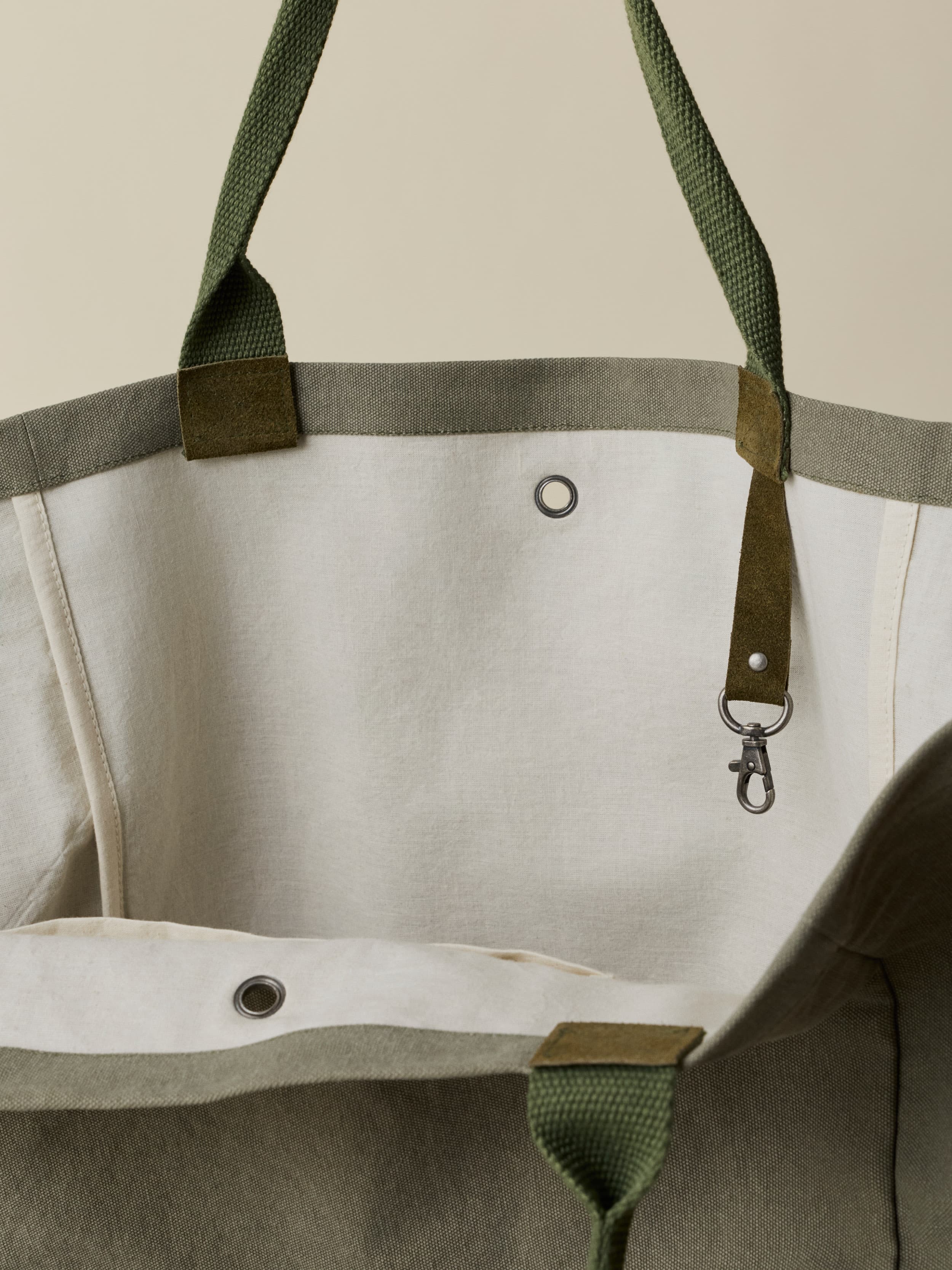 Close-up of the inside of a green bag with green straps and hardware on a neutral background