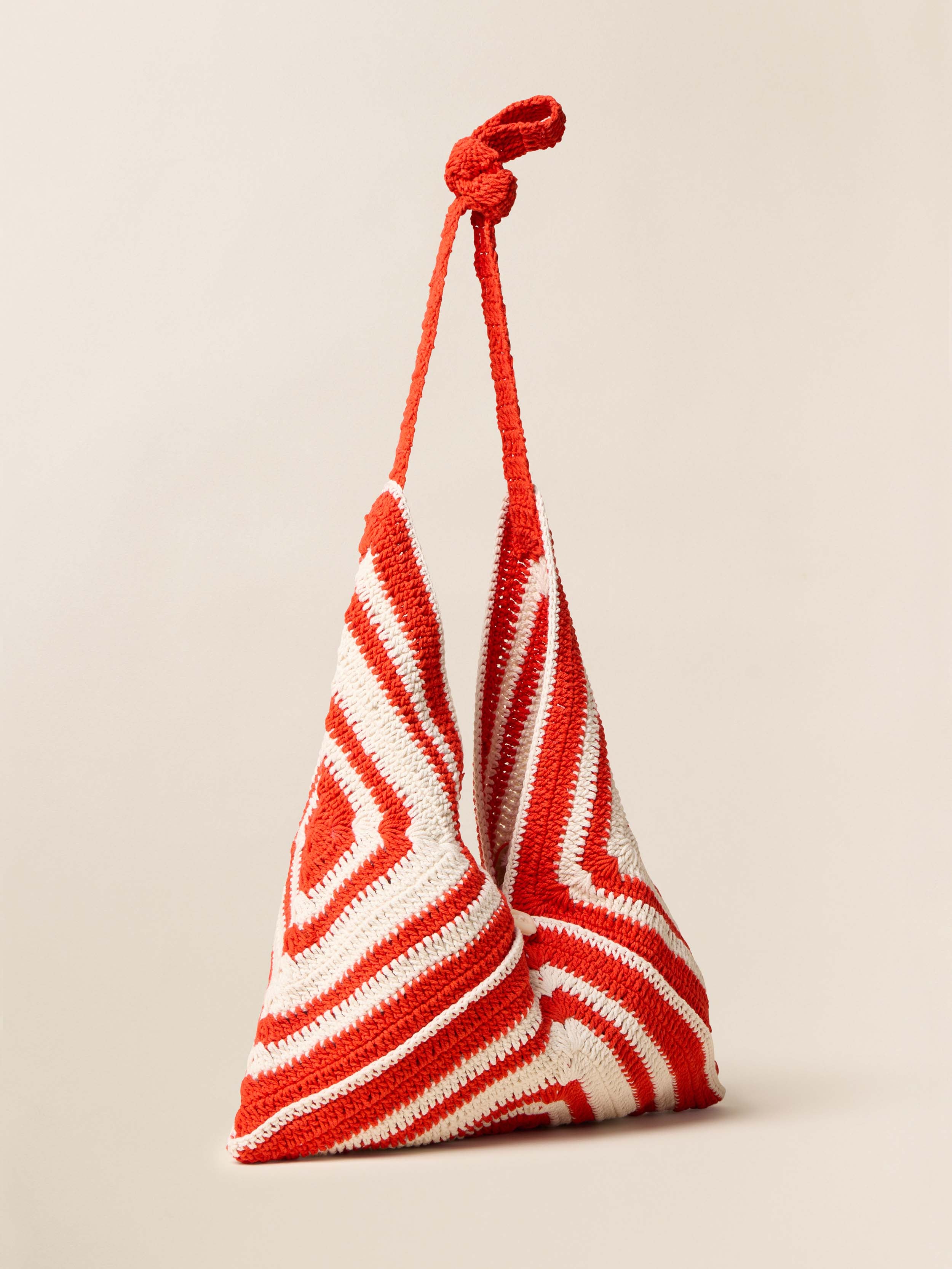 Red and white crocheted bag with a knotted handle on a beige background