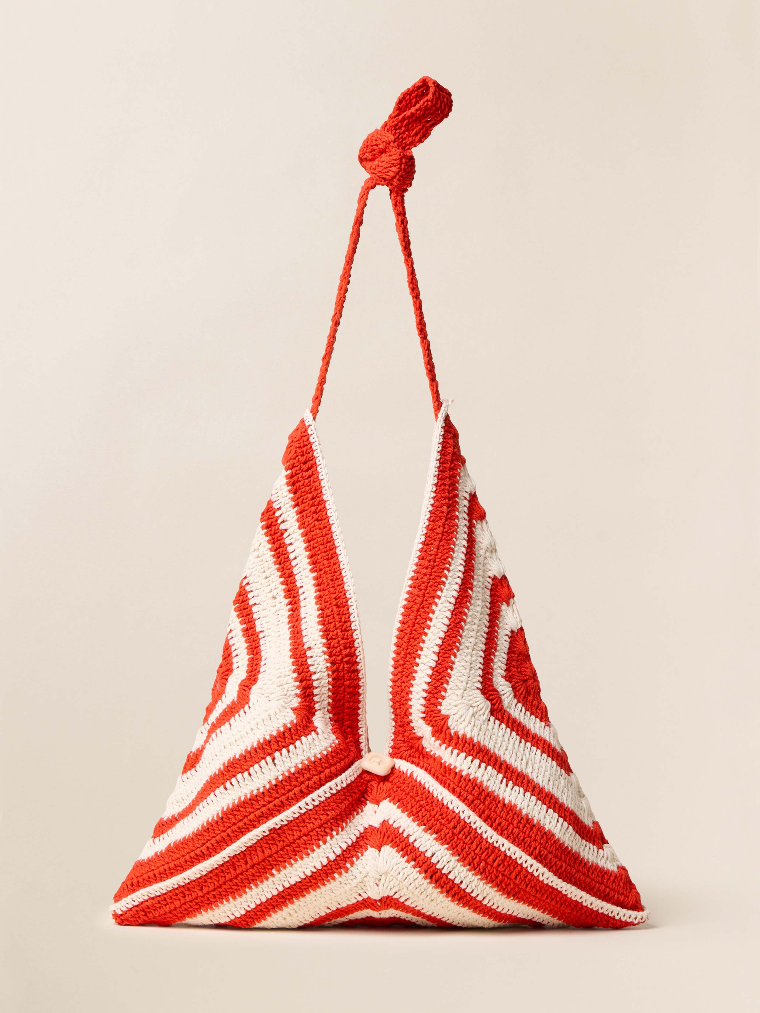 Triangular red and white crocheted bag with a rope handle on a beige background