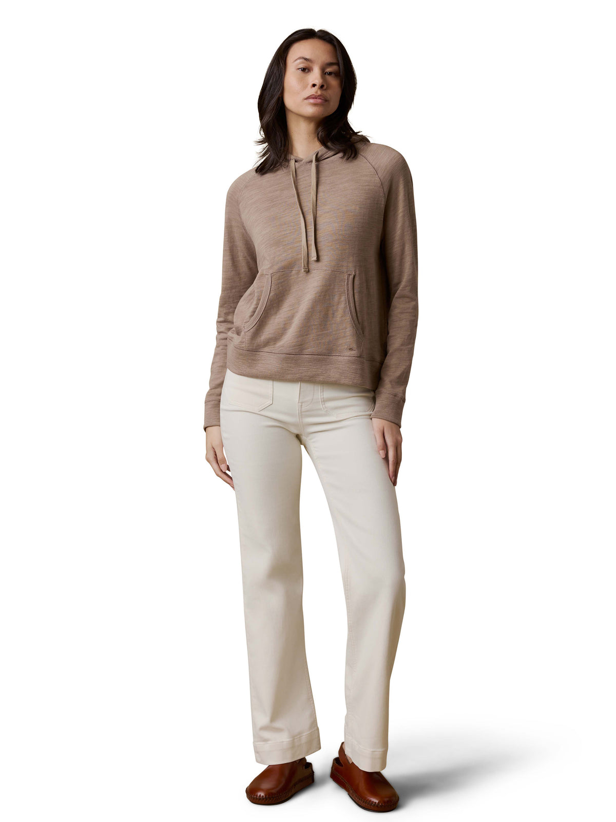 A woman wearing a beige hoodie, white pants, and brown shoes, image 2 of 3