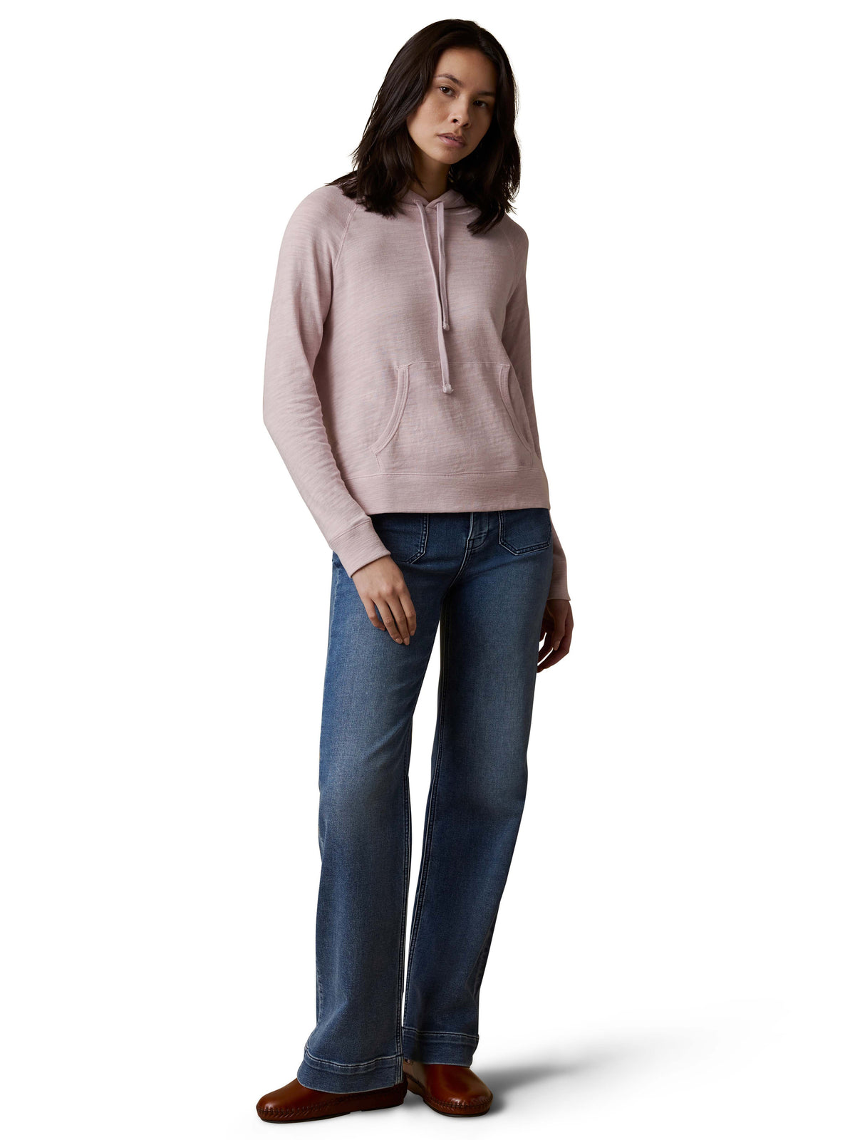 A woman wearing a light purple hoodie, blue jeans, and brown shoes, image 2 of 3