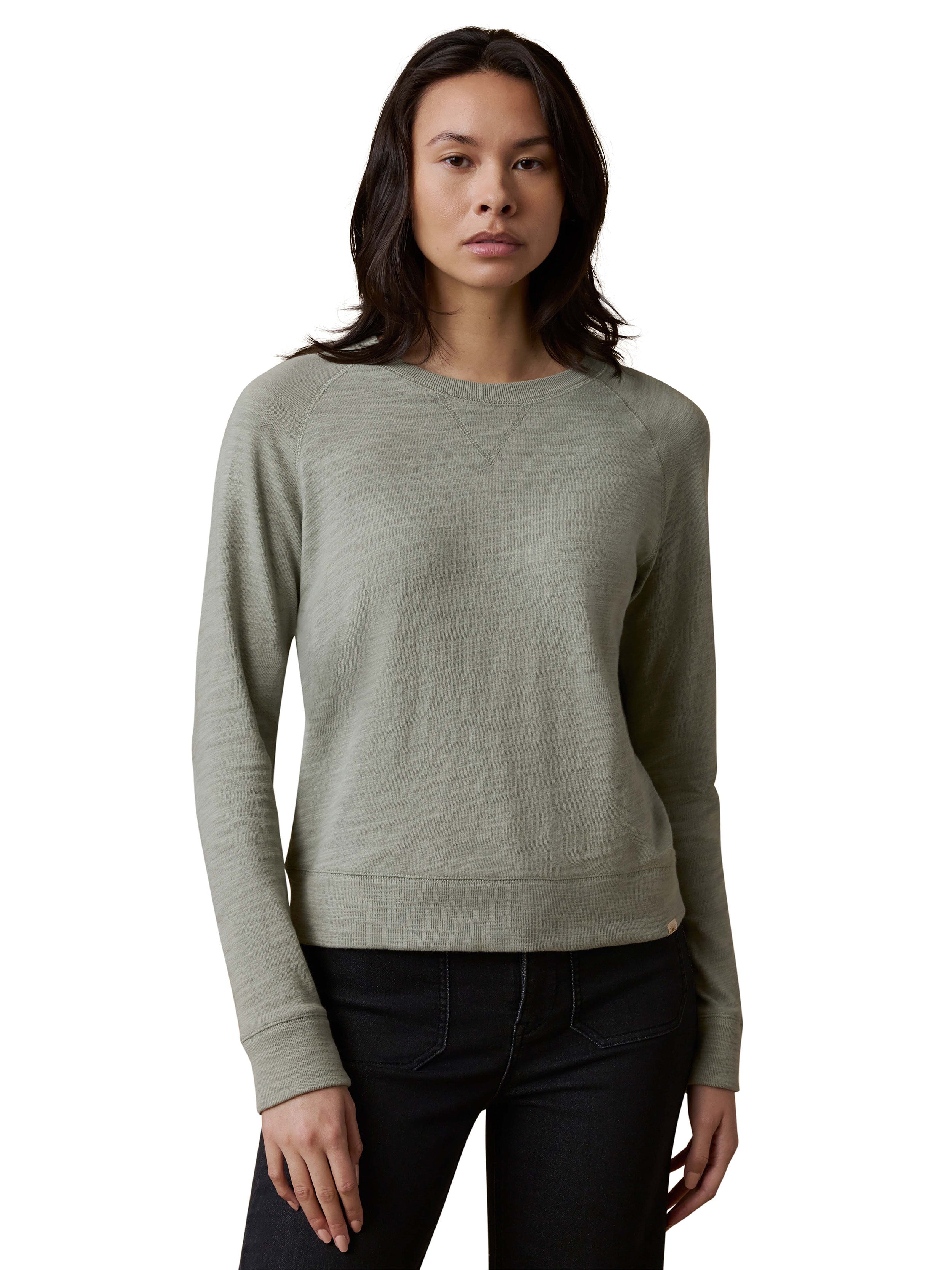 A woman wearing a sage green crewneck and dark jeans