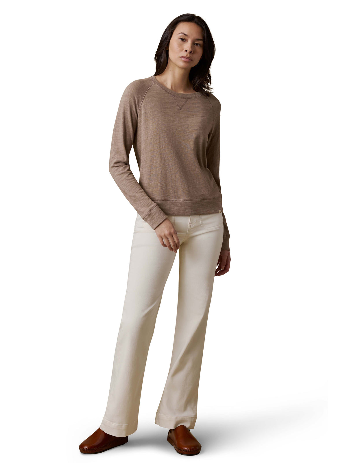 A woman wearing a beige crewneck, white pants, and brown shoes, image 2 of 3