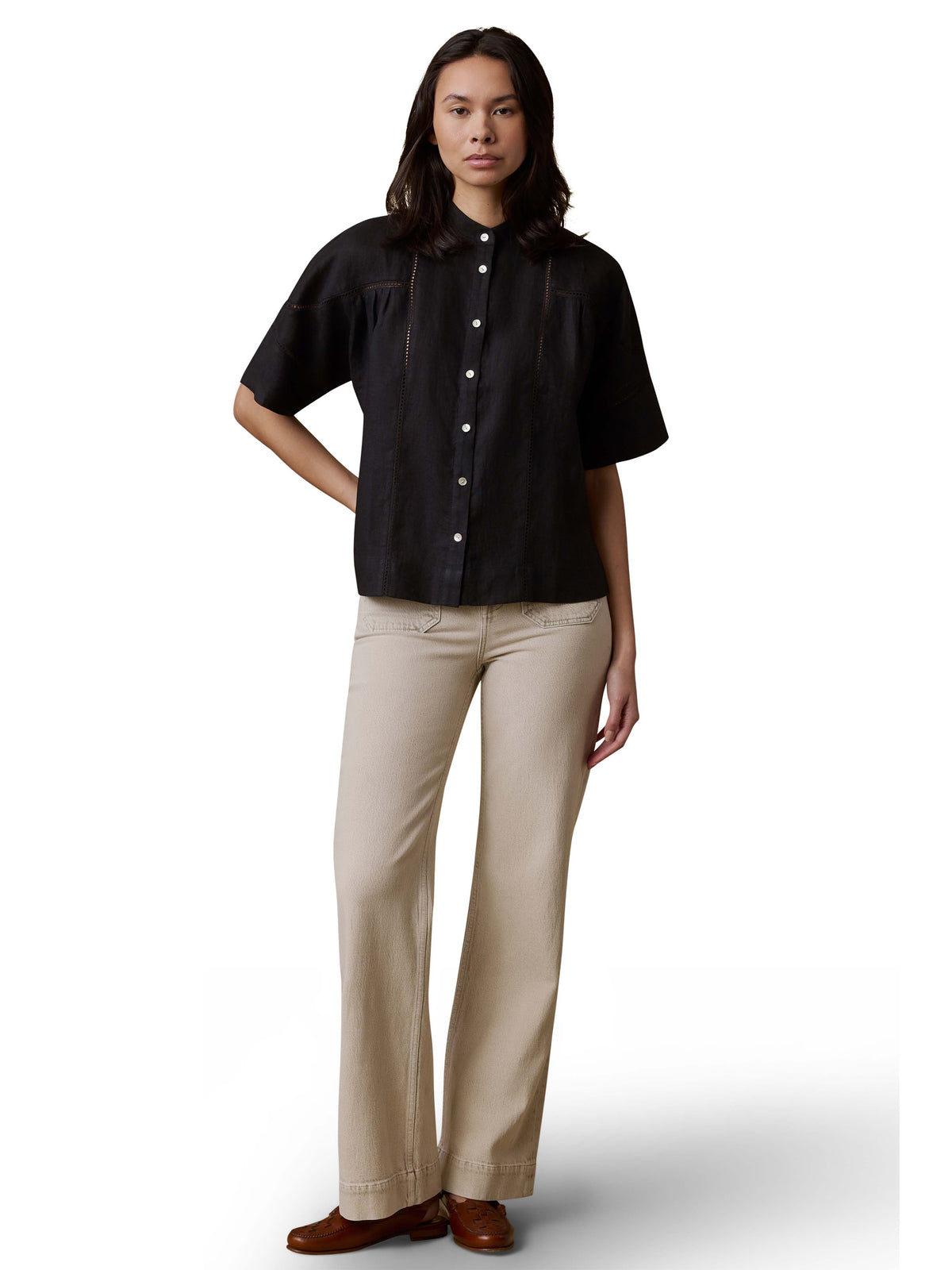 A woman wearing a black shirt, beige pants, and brown shoes, image 2 of 3