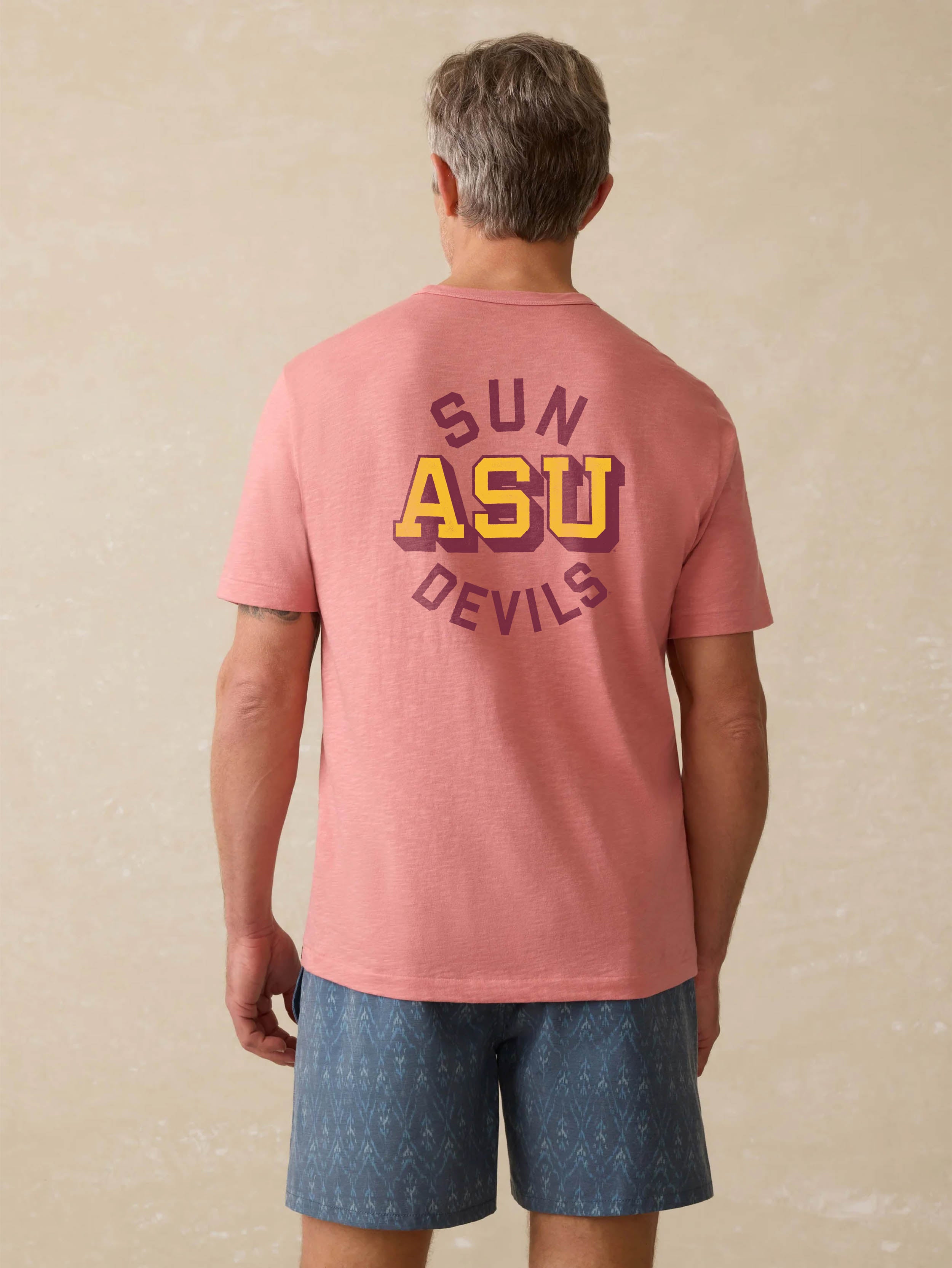 Man wearing a red shirt with Arizona State University graphic on the center back against a beige background