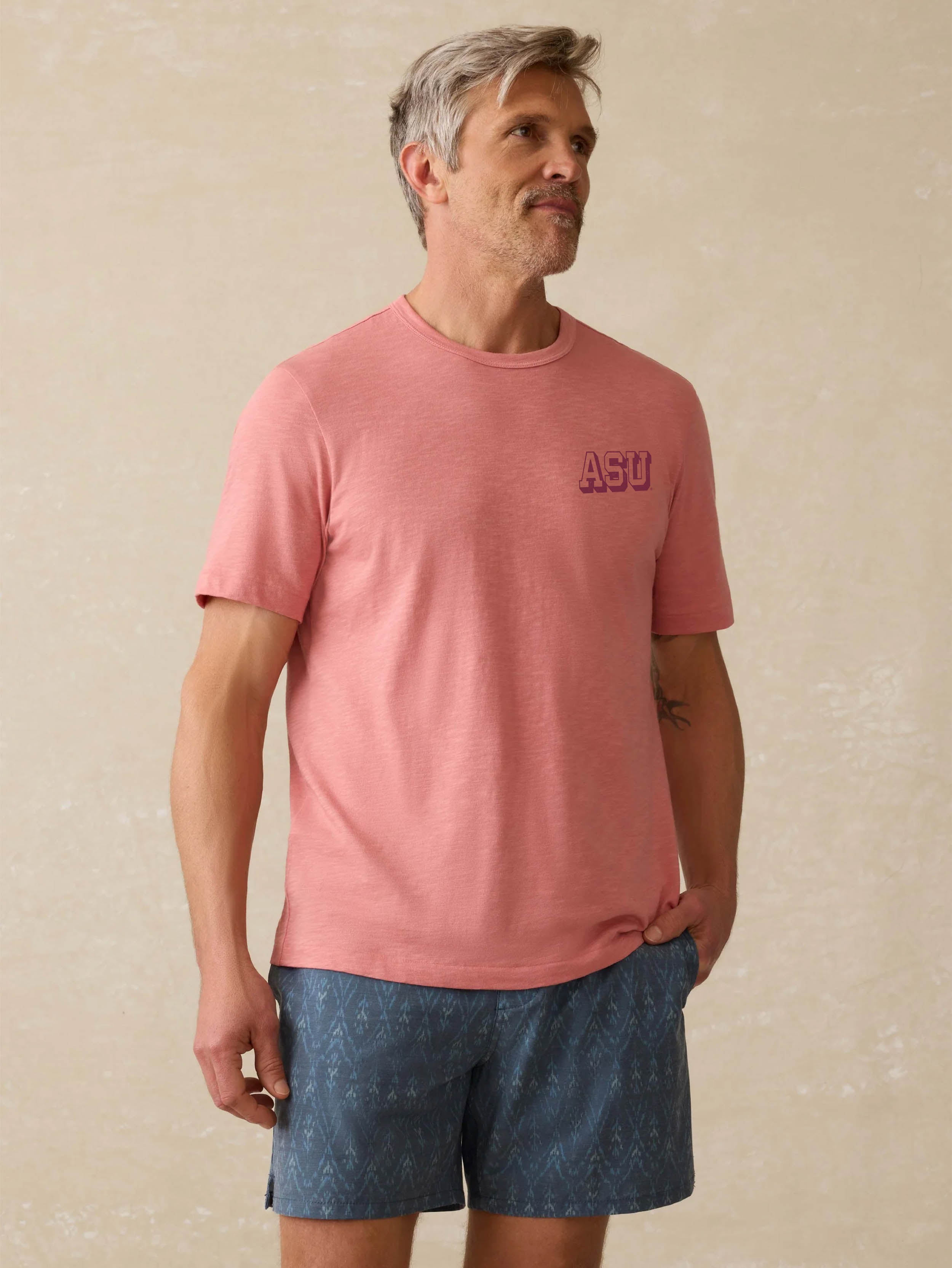 Man wearing a red shirt with Arizona State University graphic on the left chest against a beige background