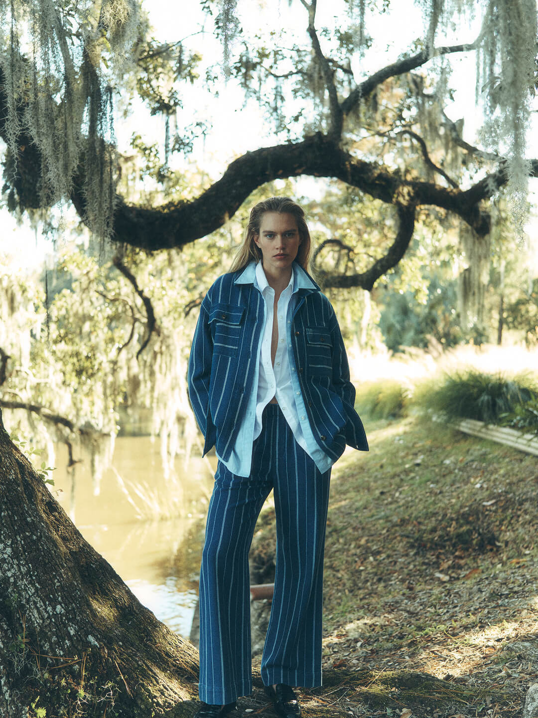 female model in southern low country landscape surrounded by a pond and Spanish moss, wearing a indigo striped jacket and pants, paired with a chambray shirt