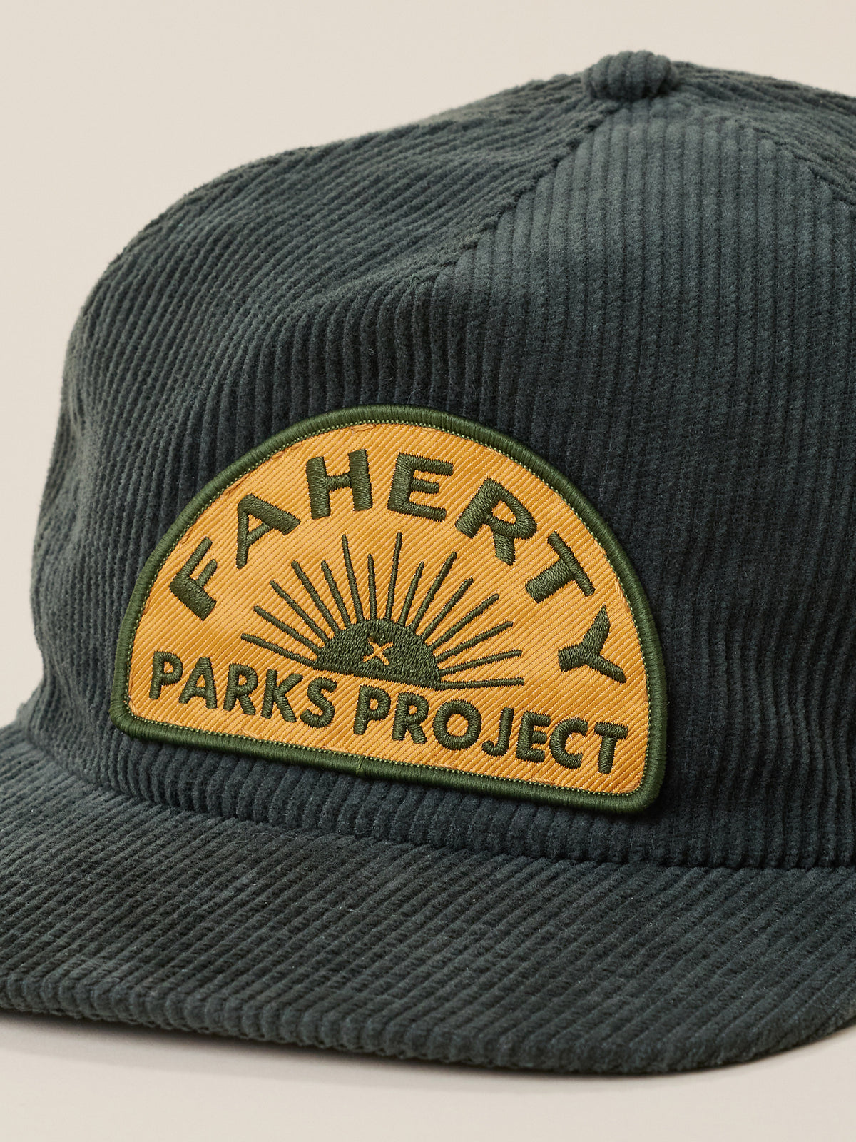 A close-up of a dark green corduroy baseball cap featuring a prominent yellow and green embroidered patch on the front that reads 'FAHERTY x PARKS PROJECT'., image 2 of 3