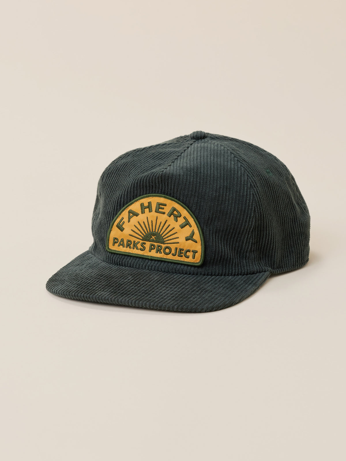 A dark green corduroy baseball cap with a curved yellow patch on the front that reads 'FAHERTY x PARKS PROJECT' with a sunburst design, set against a solid beige background., image 1 of 3