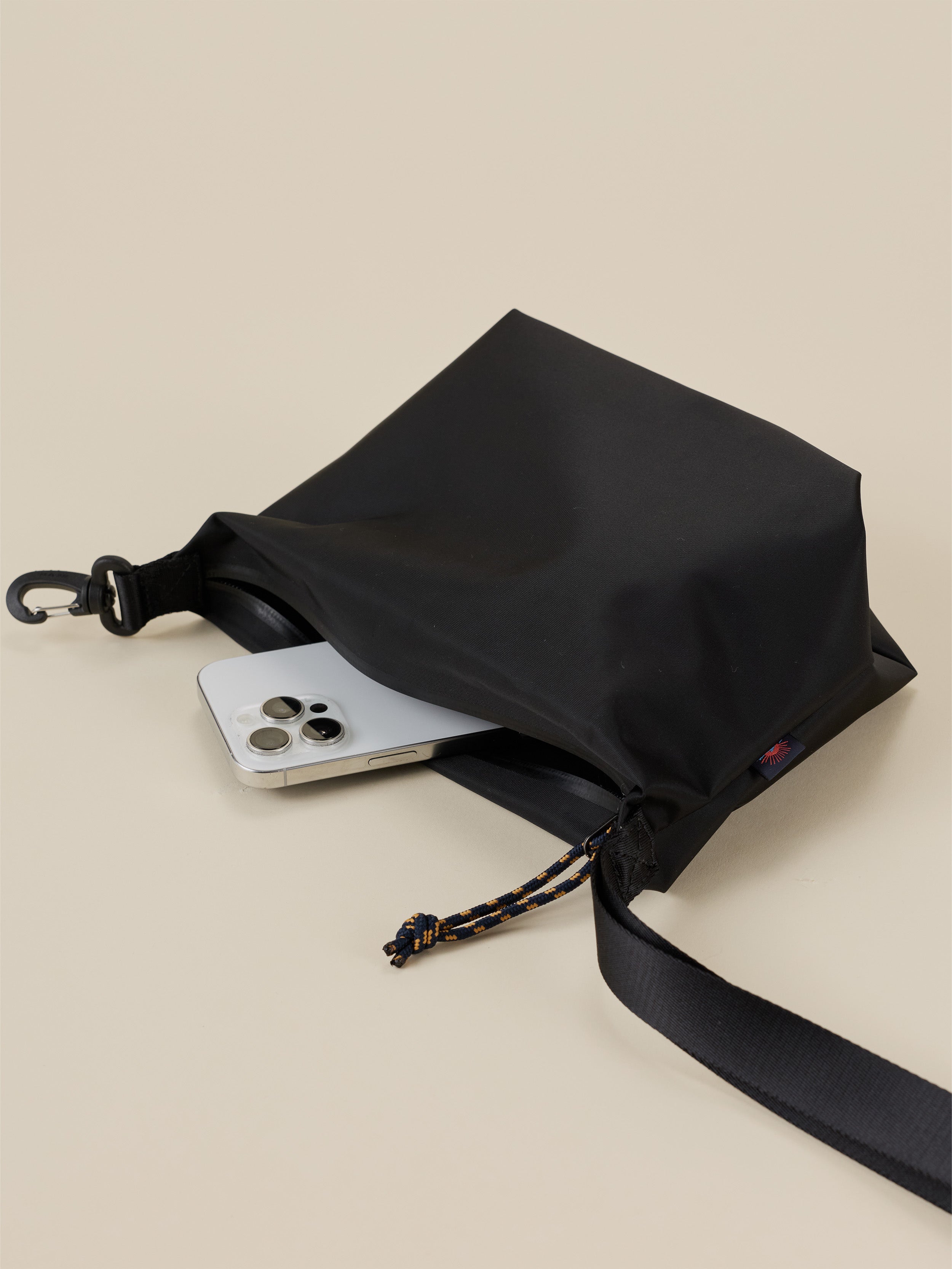 Black dry bag with a phone inside on a beige background