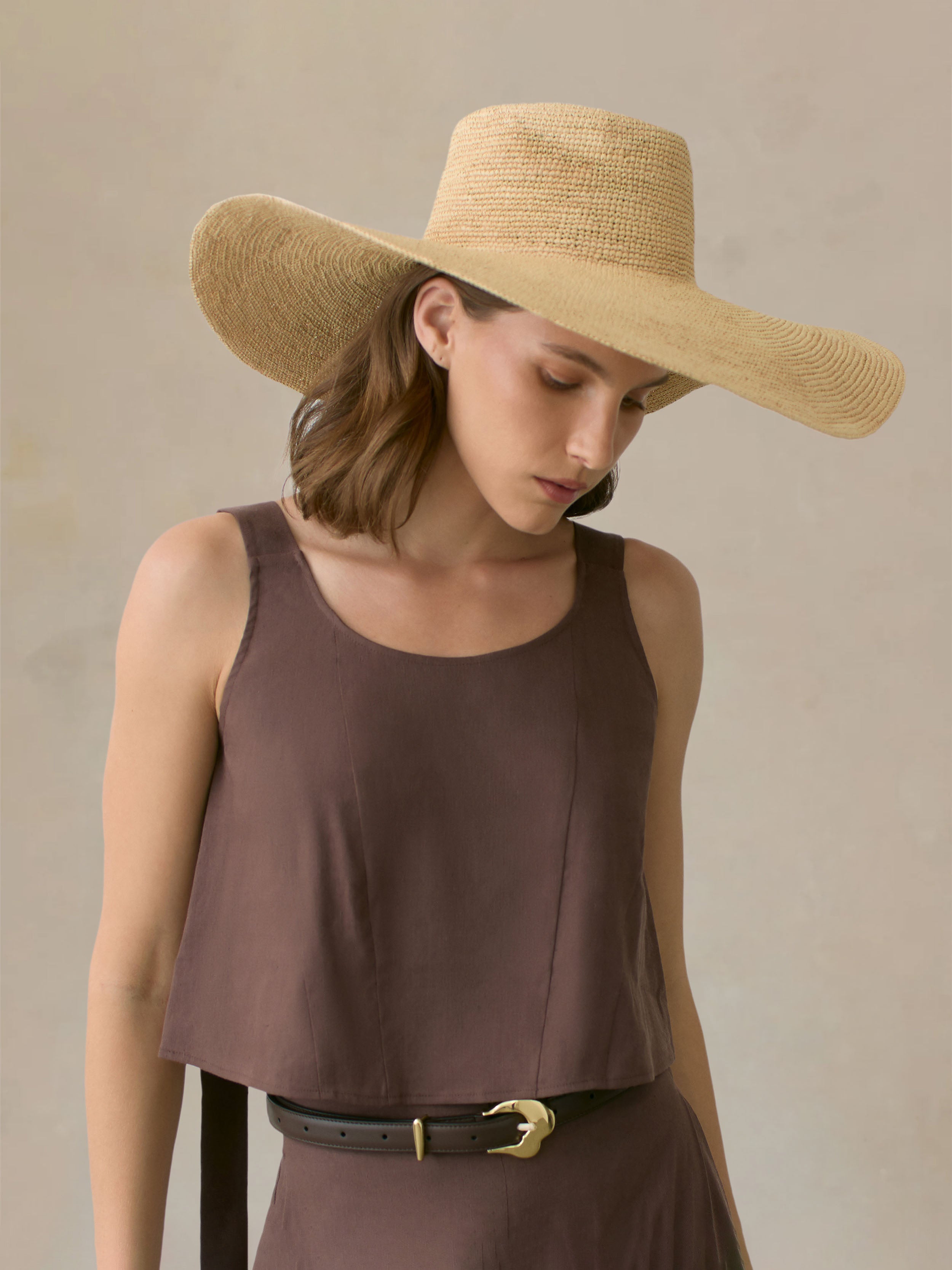Woman wearing a straw hat and brown outfit against a beige background