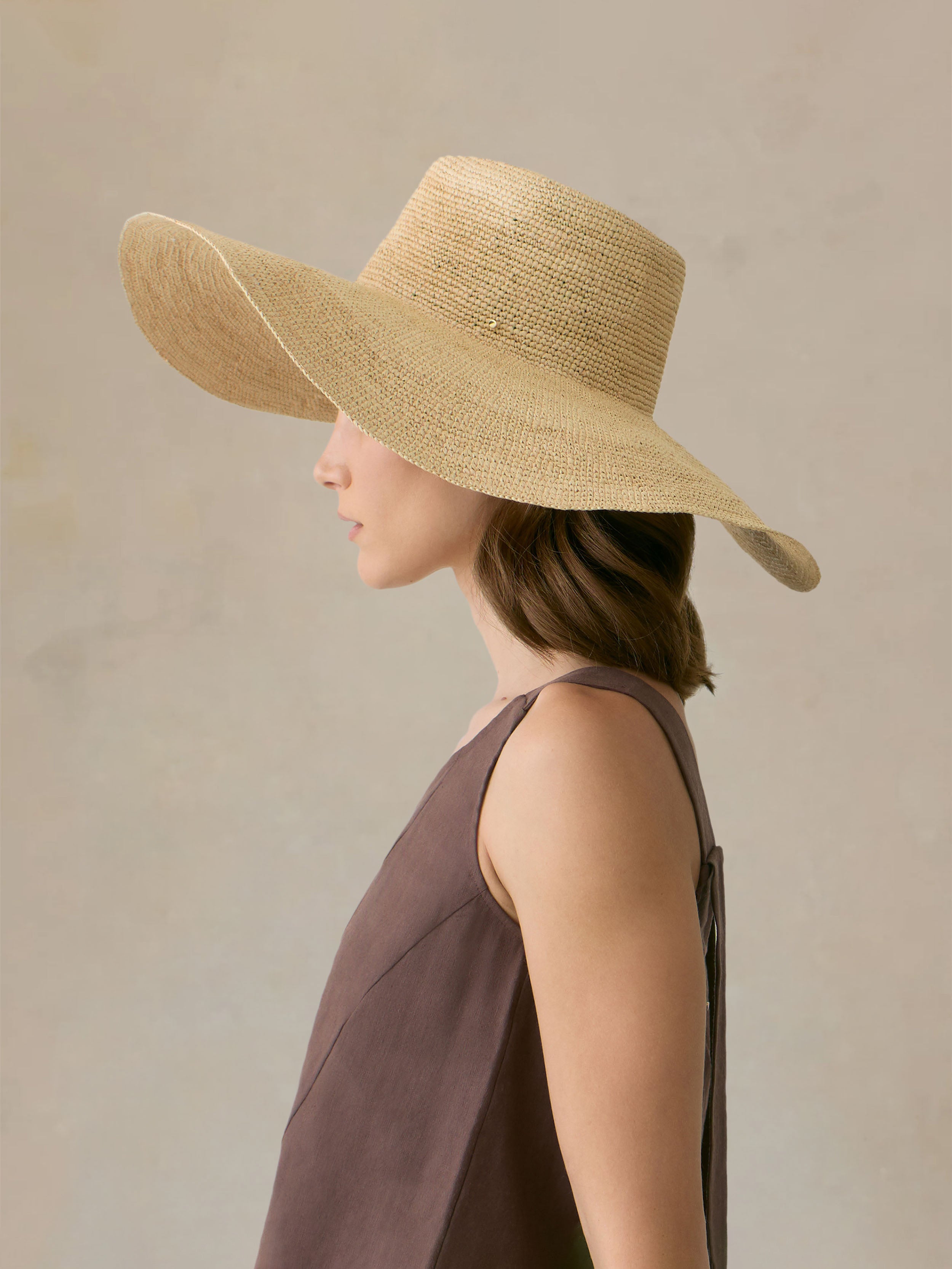 Woman wearing a straw hat and brown outfit against a beige background