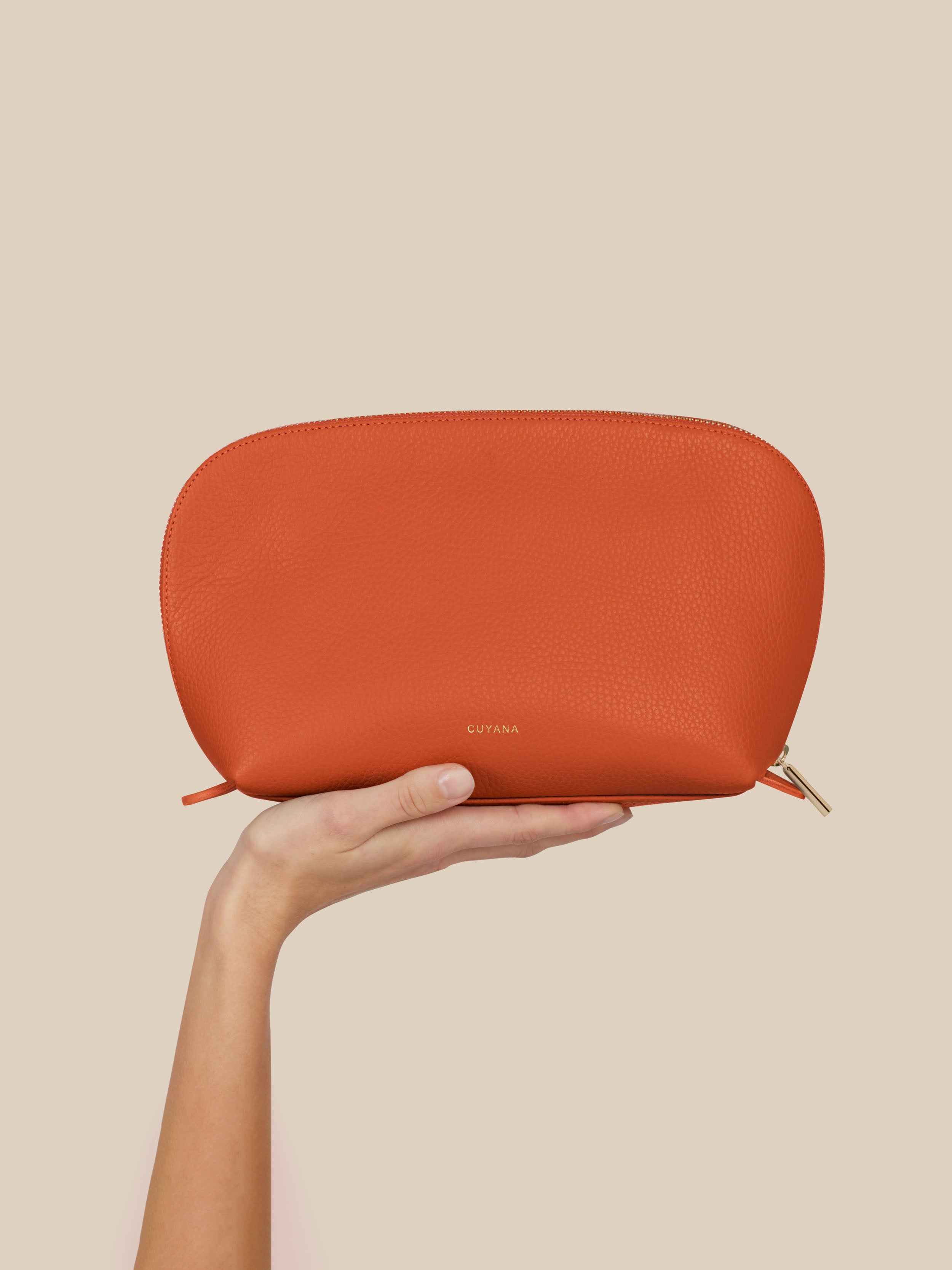 Orange cosmetic pouch held by a hand against a beige background