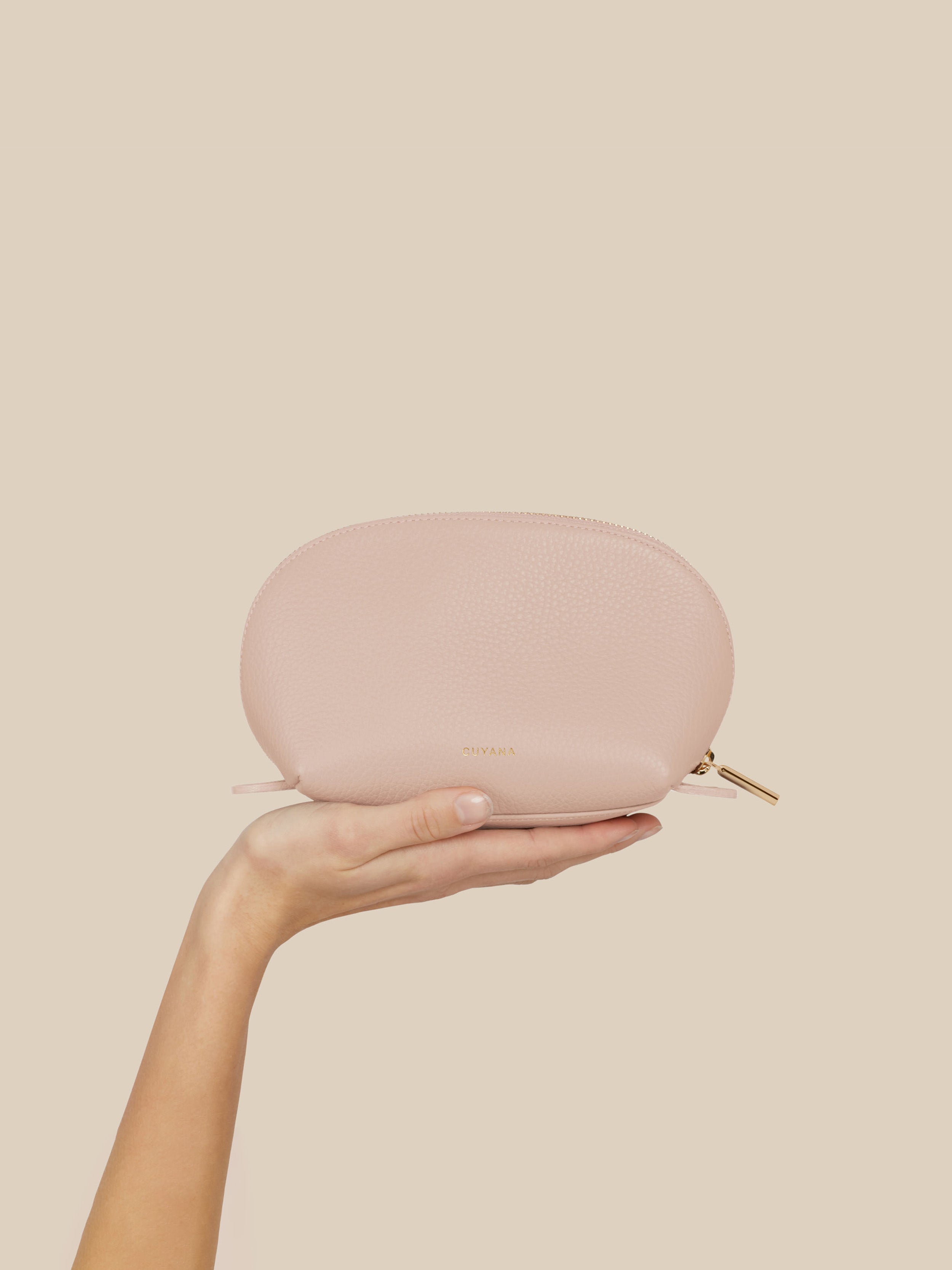 Hand holding a pink cosmetic pouch against a beige background