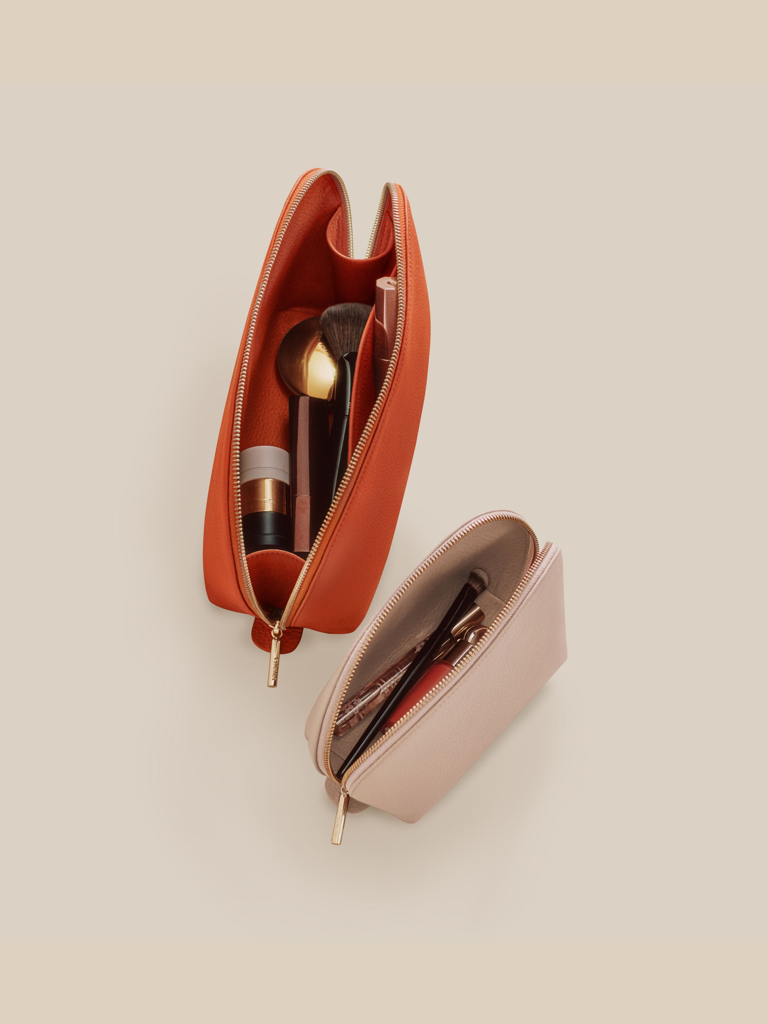 Two open cosmetic bags, one orange and one pink, containing makeup items on a beige background.