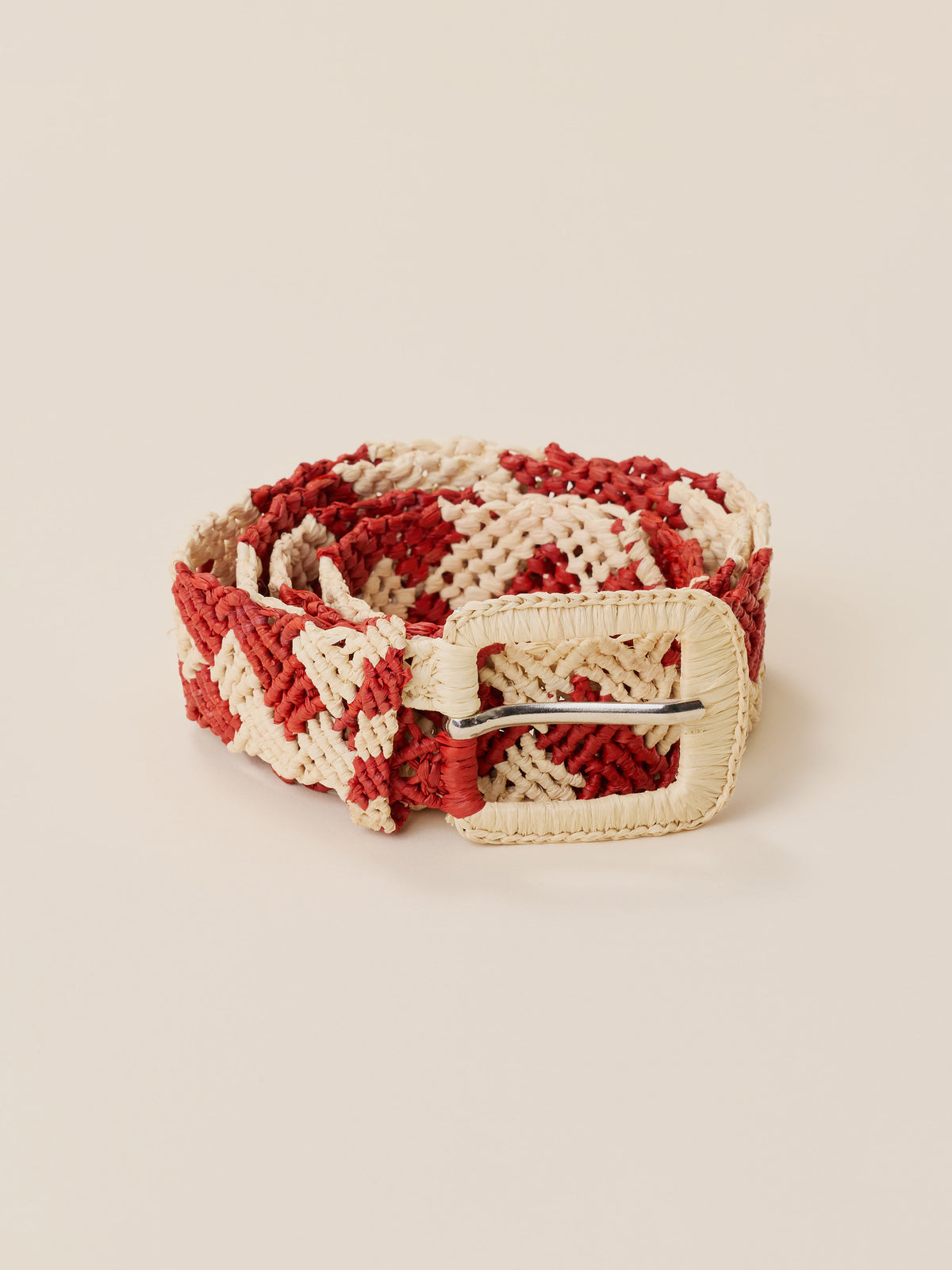 A woven belt with a red and cream chevron pattern and a cream buckle, displayed on a solid beige background., image 1 of 2