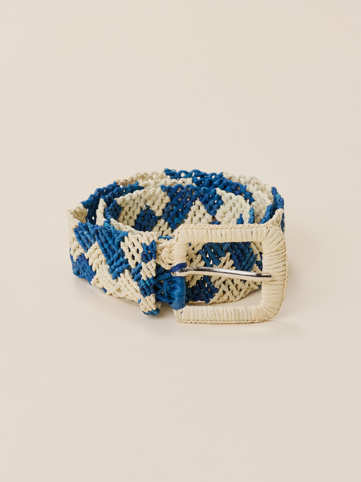 A woven belt with a blue and cream geometric pattern and a cream-colored buckle, displayed on a solid beige background., image 1 of 2
