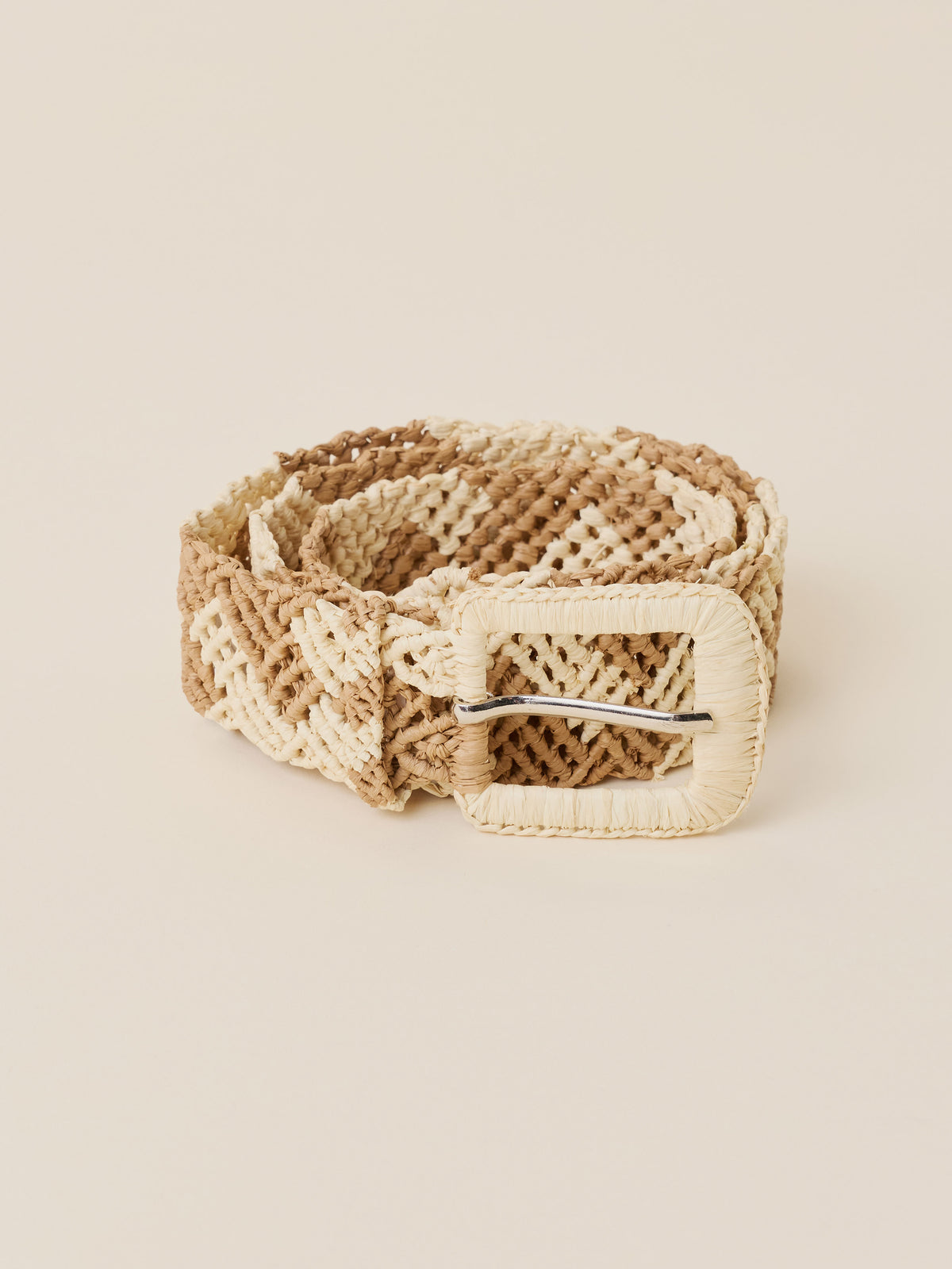 A woven belt with a textured geometric pattern in beige and cream, featuring a large cream-colored buckle with a silver metal bar, set against a solid light beige background., image 1 of 2
