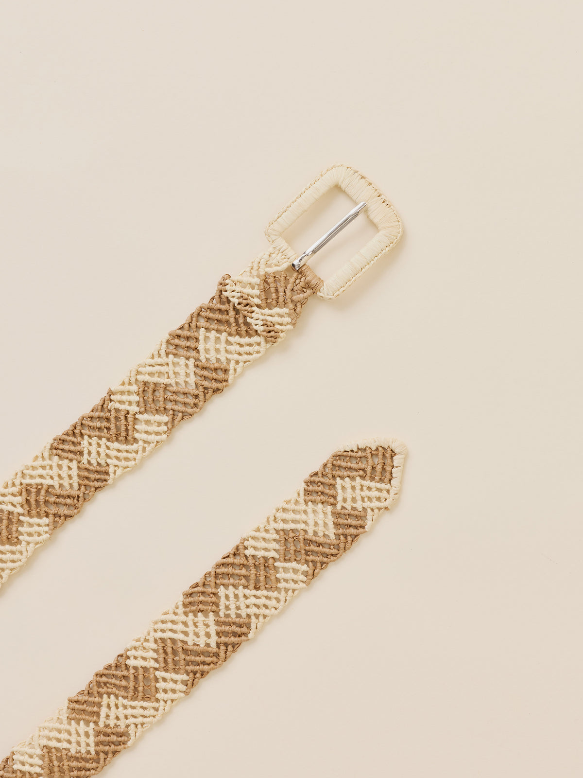 A woven belt with a textured herringbone pattern in beige and brown, featuring a cream-colored rectangular buckle, laid out diagonally on a solid cream background., image 2 of 2