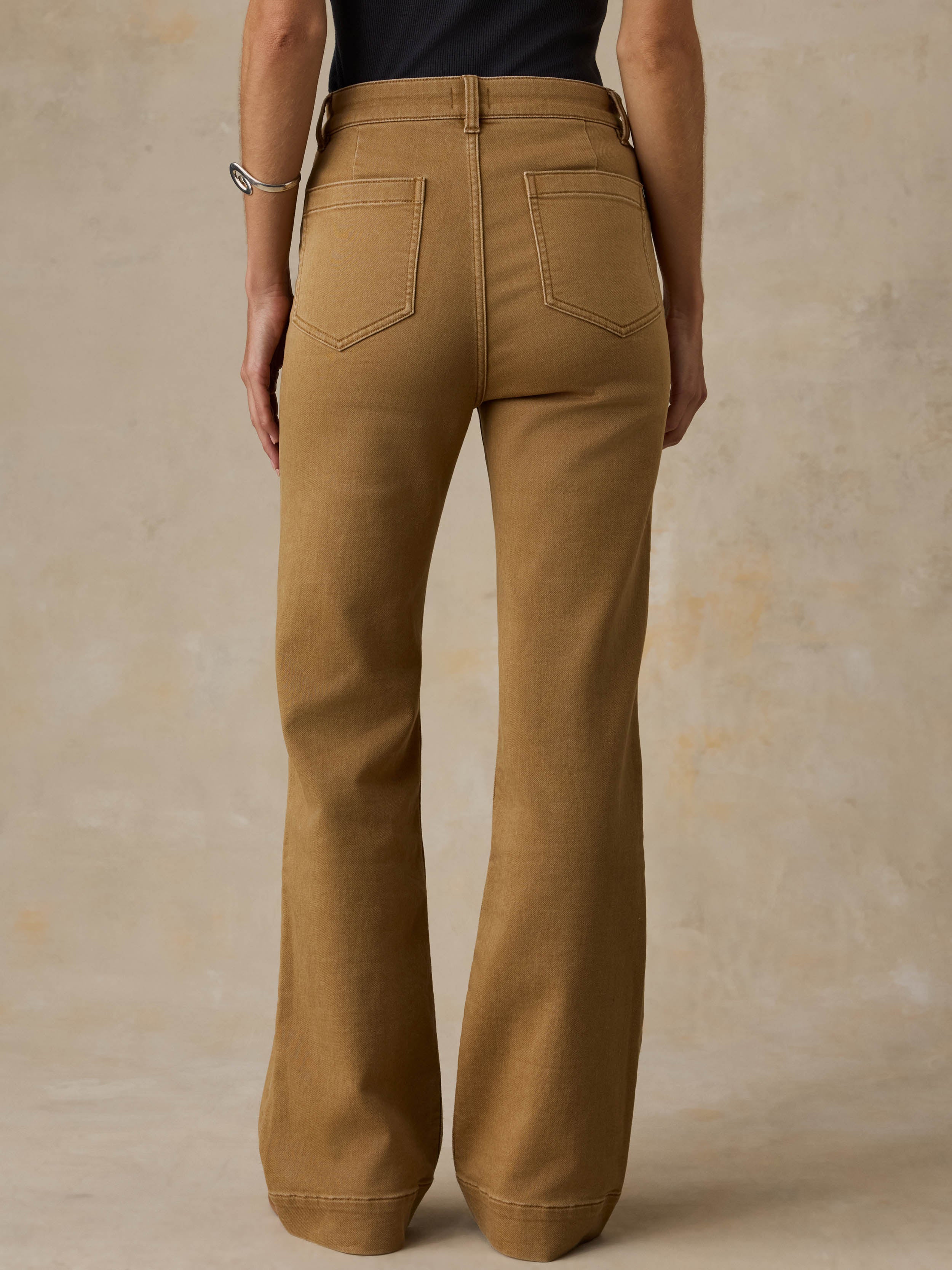 Woman wearing a black tank top and brown pants against a beige background
