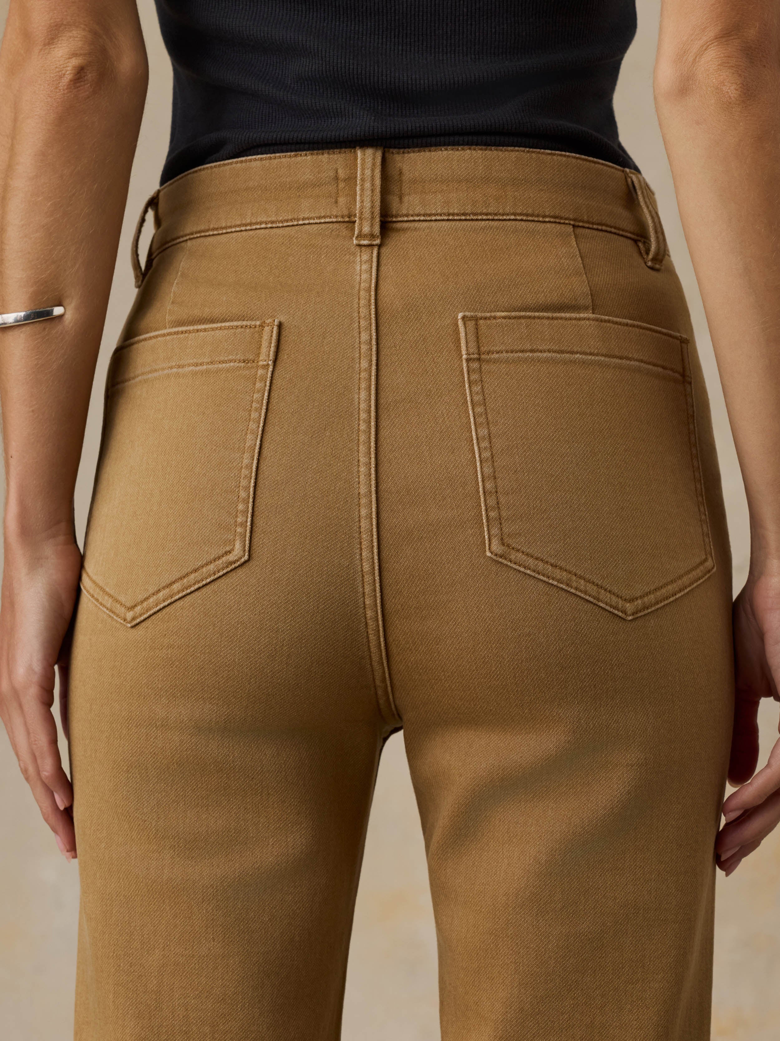 Woman wearing a black tank top and brown pants against a beige background