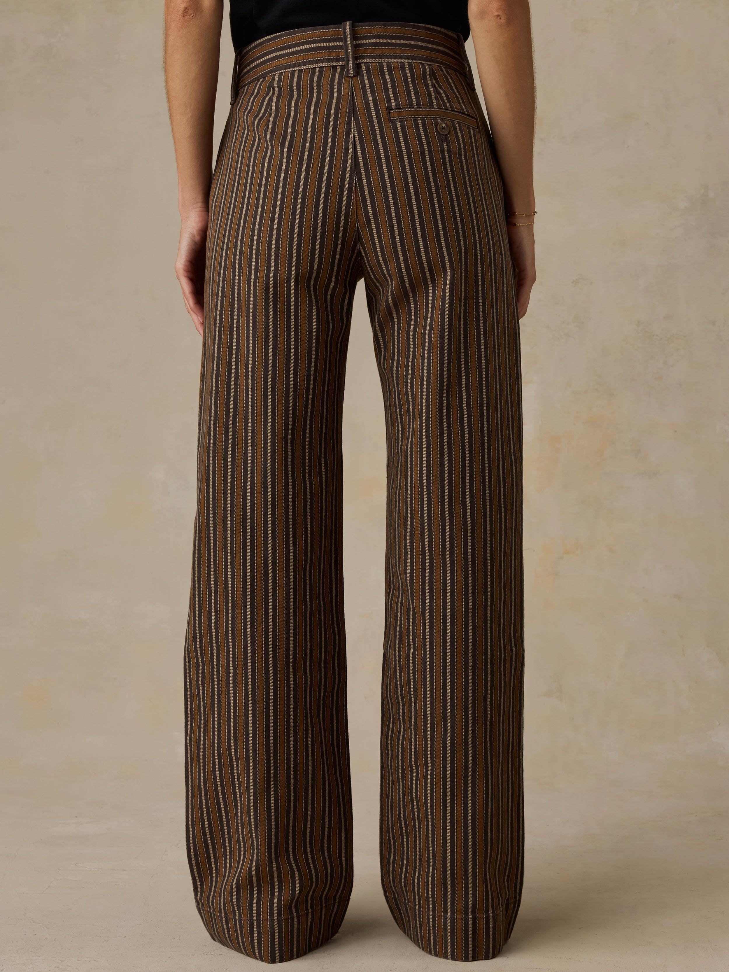 Woman wearing a black t-shirt and brown striped pants on a beige background