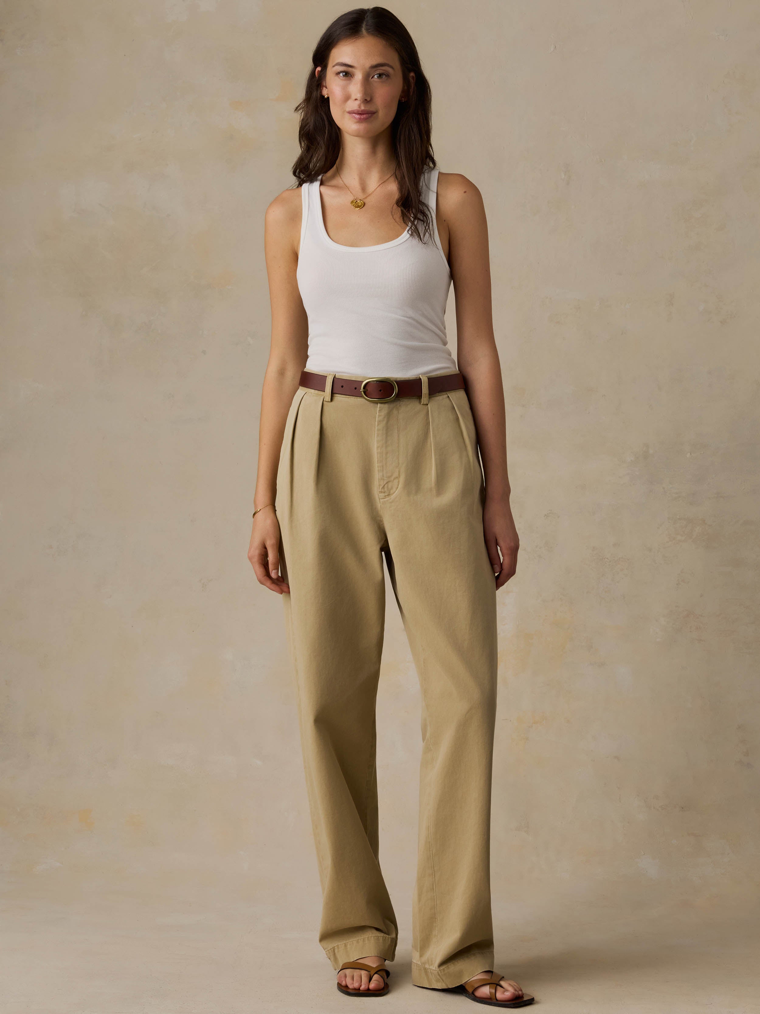 Woman wearing a white tank top and beige pants against a beige background