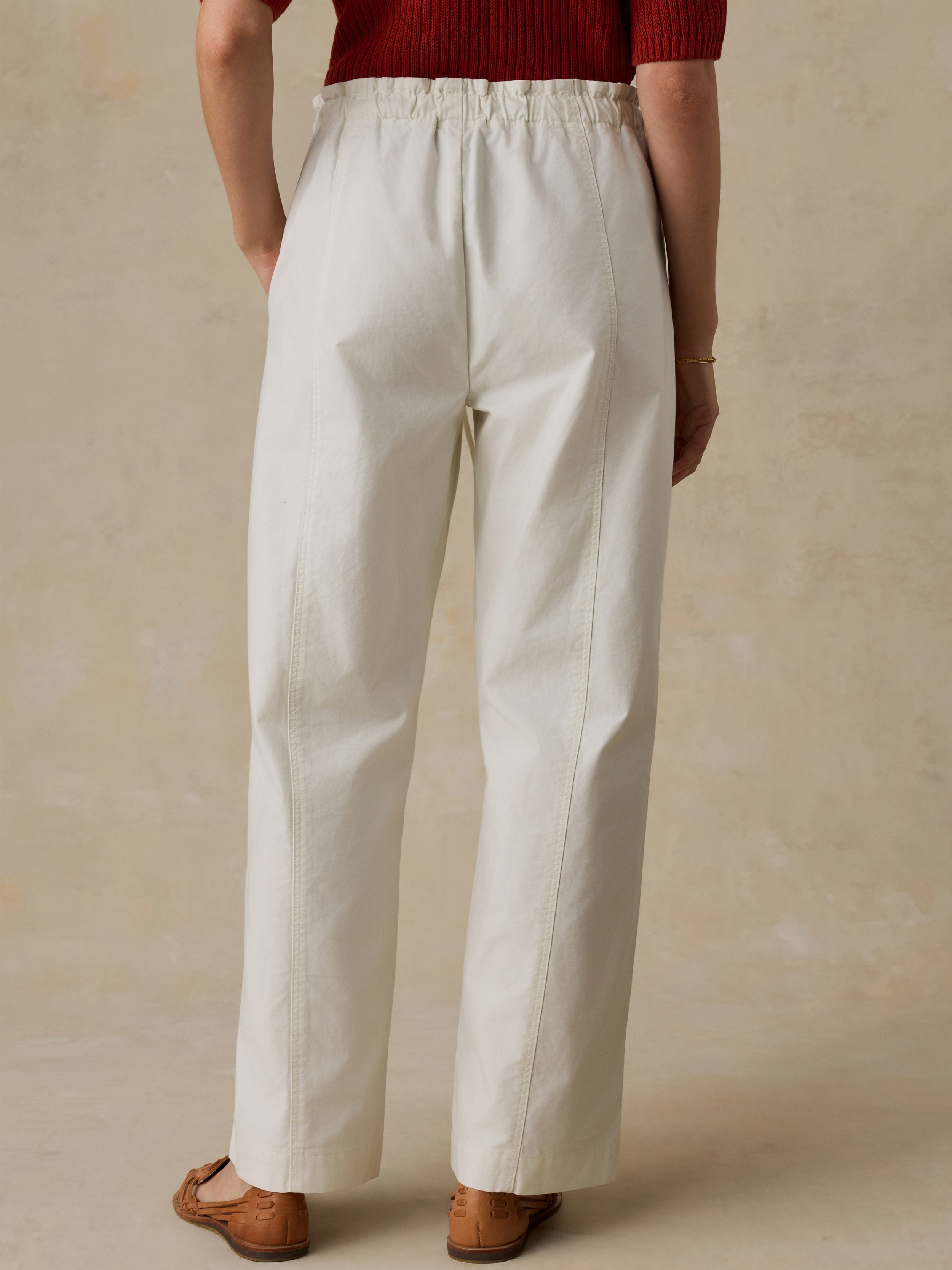 Woman wearing a red knit polo shirt and white drawstring pants against a beige background