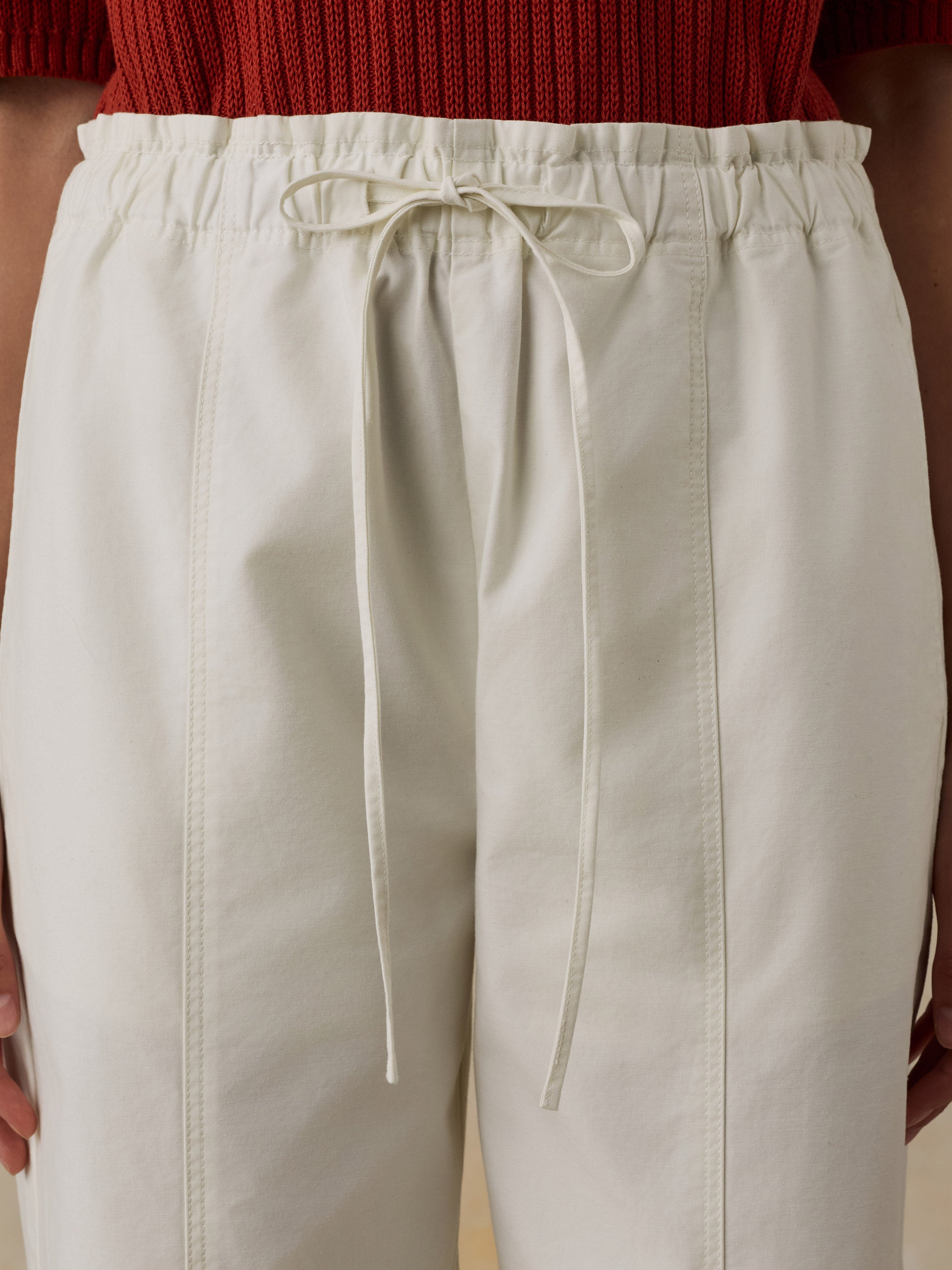 Woman wearing a red knit polo shirt and white drawstring pants against a beige background