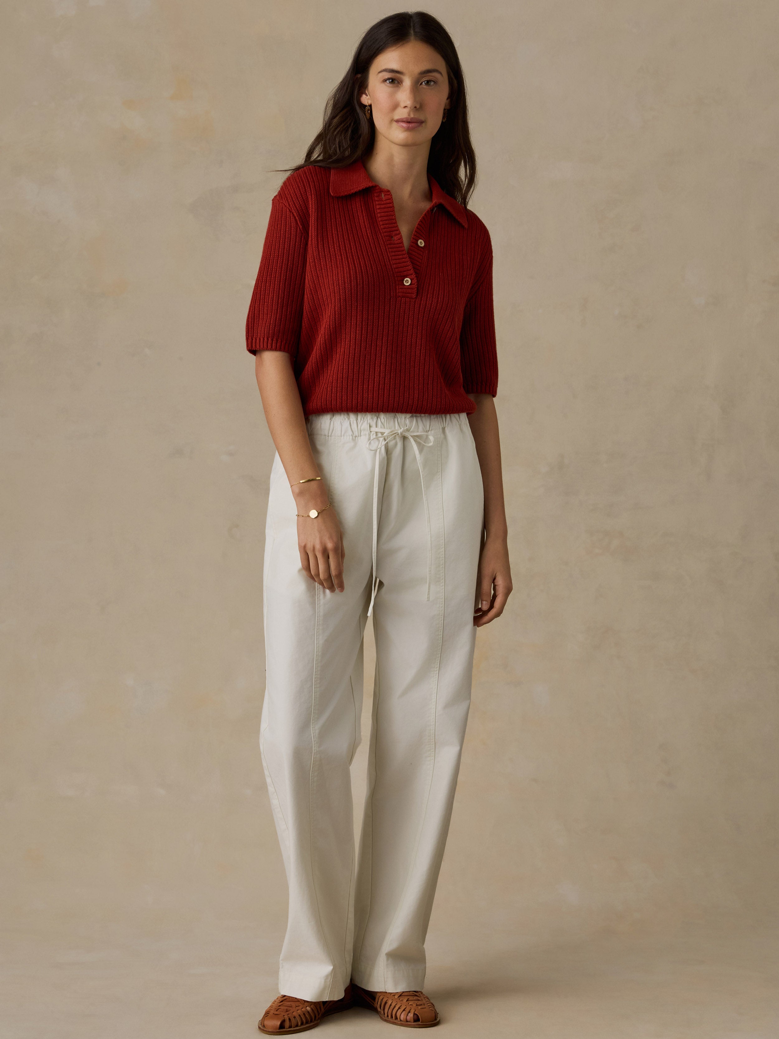 Woman wearing a red knit polo shirt and white drawstring pants against a beige background