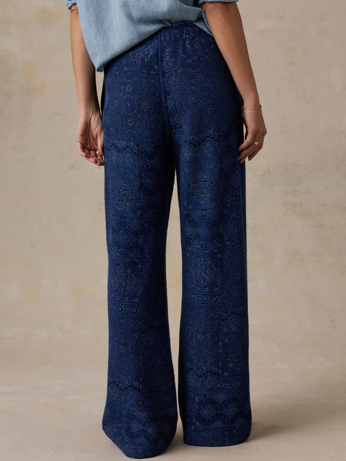 Woman wearing a printed pair of blue pants standing against a beige studio background, image 4 of 7