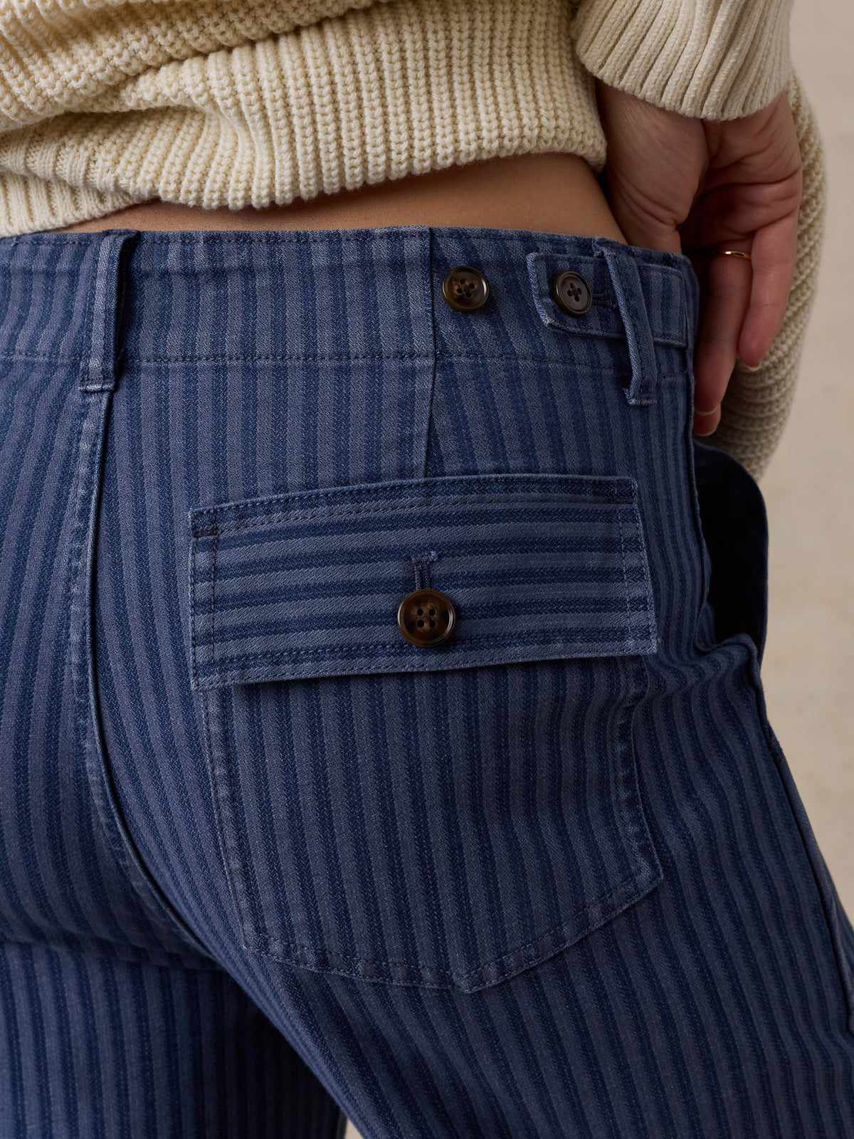 Close-up of a person wearing blue pinstriped jeans, showing the back pocket, button closure, and ribbed cream sweater., image 2 of 6