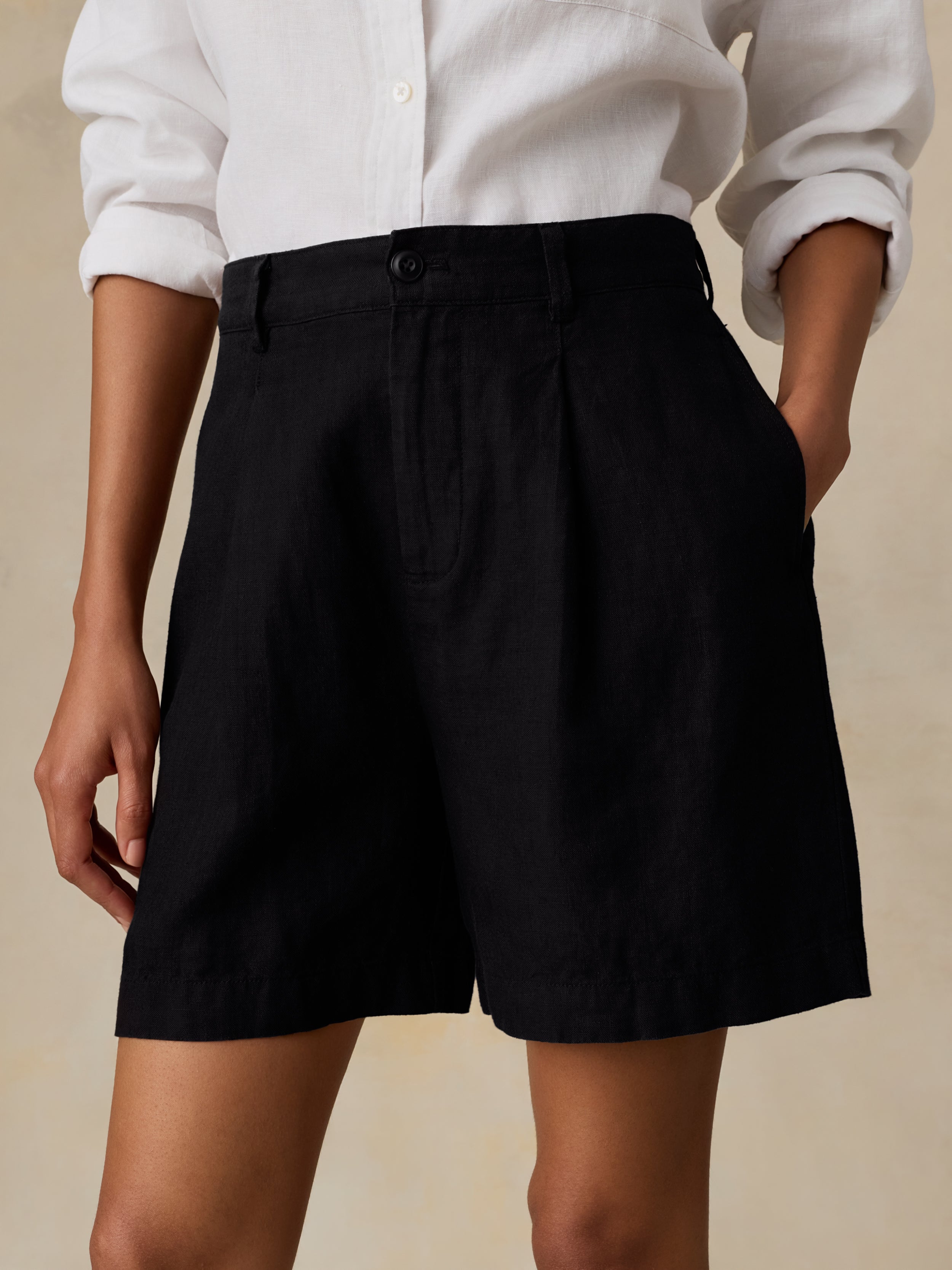 Woman wearing a white shirt and black linen shorts against a beige background