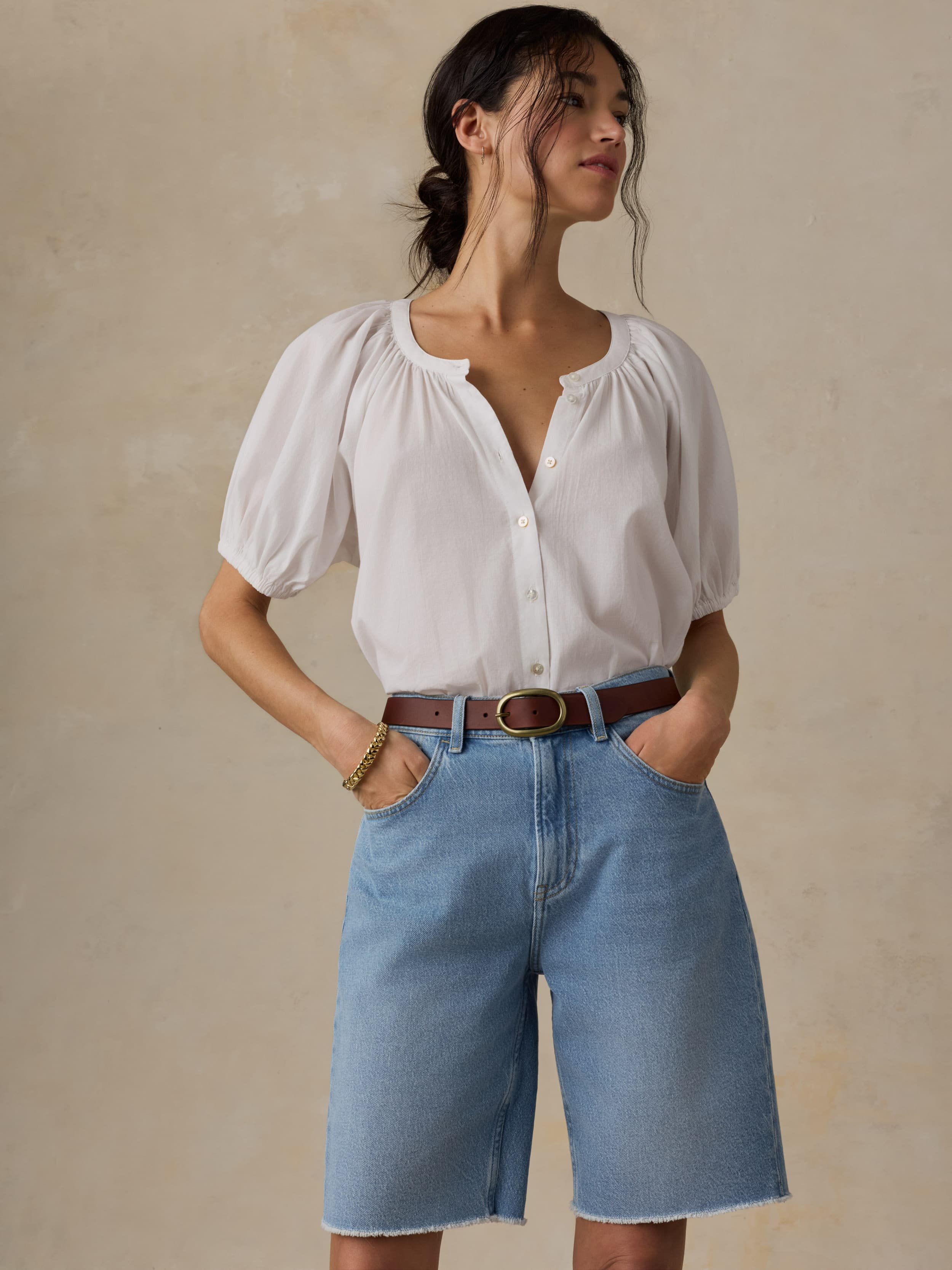 Woman wearing a white blouse and blue denim shorts against a beige background
