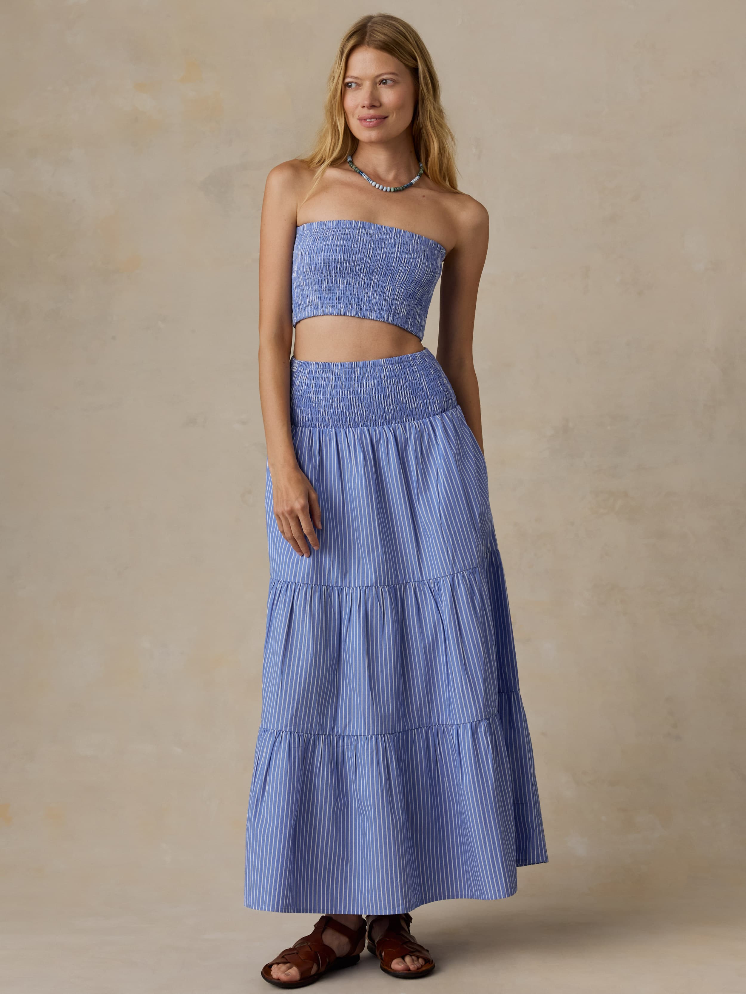Woman is wearing a striped maxi skirt and matching bandeau top against a beige background