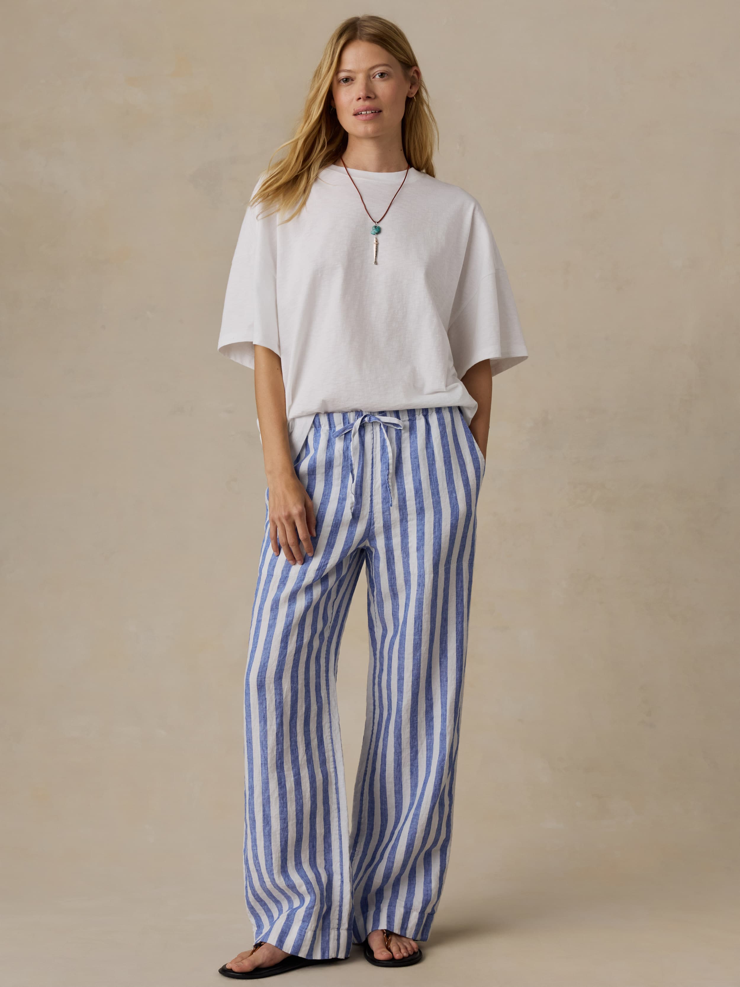 Woman wearing a white t-shirt and blue striped pants against a beige background