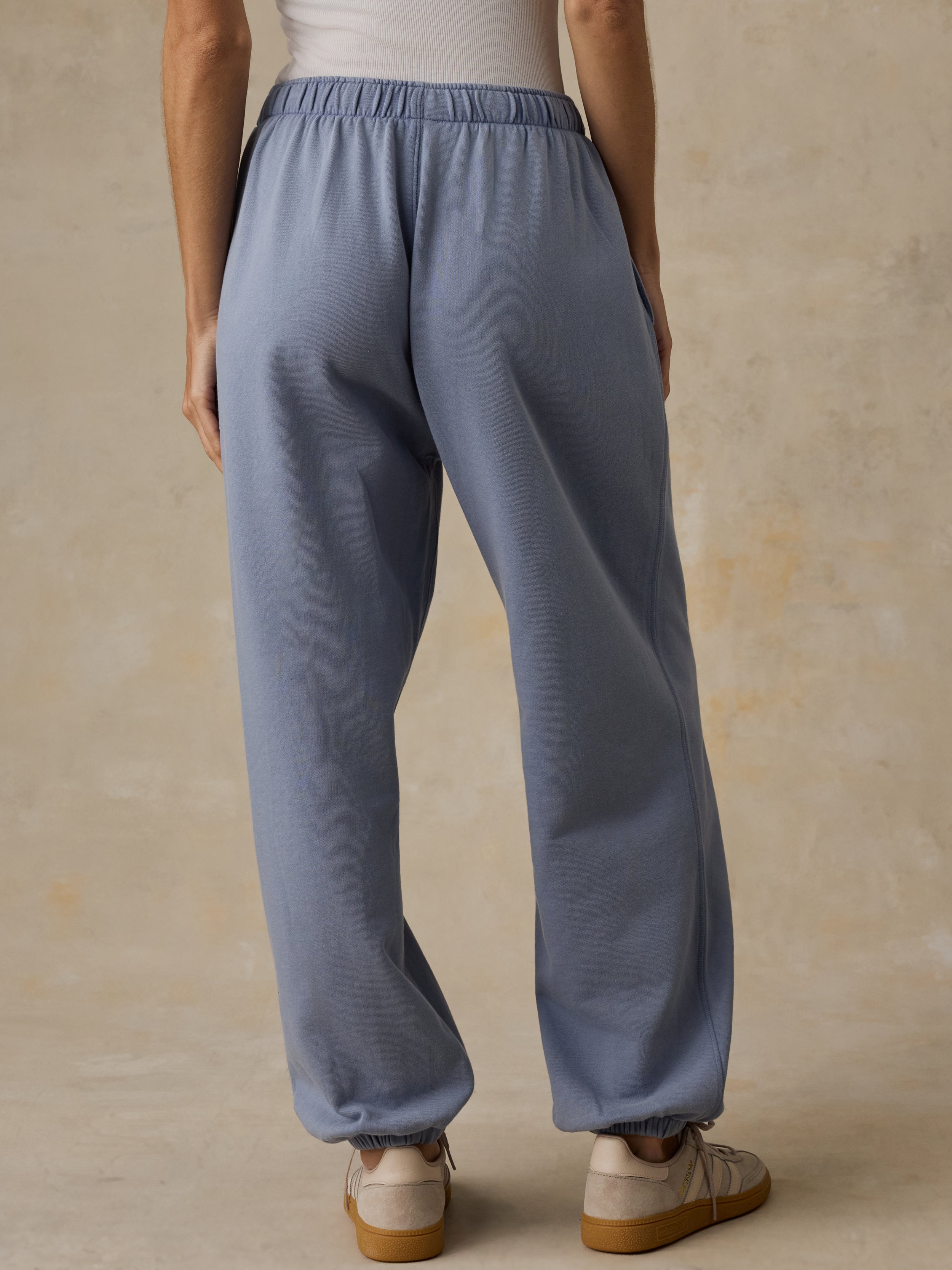 Woman wearing a white tank top and blue sweatpants against a beige background
