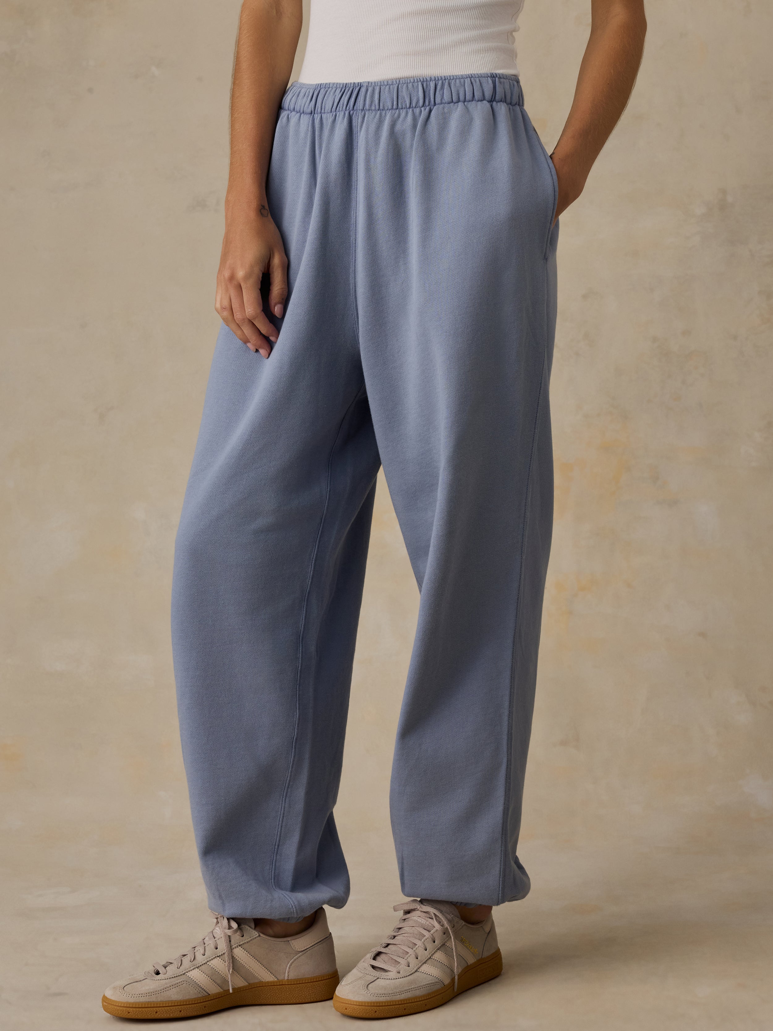 Woman wearing a white tank top and blue sweatpants against a beige background