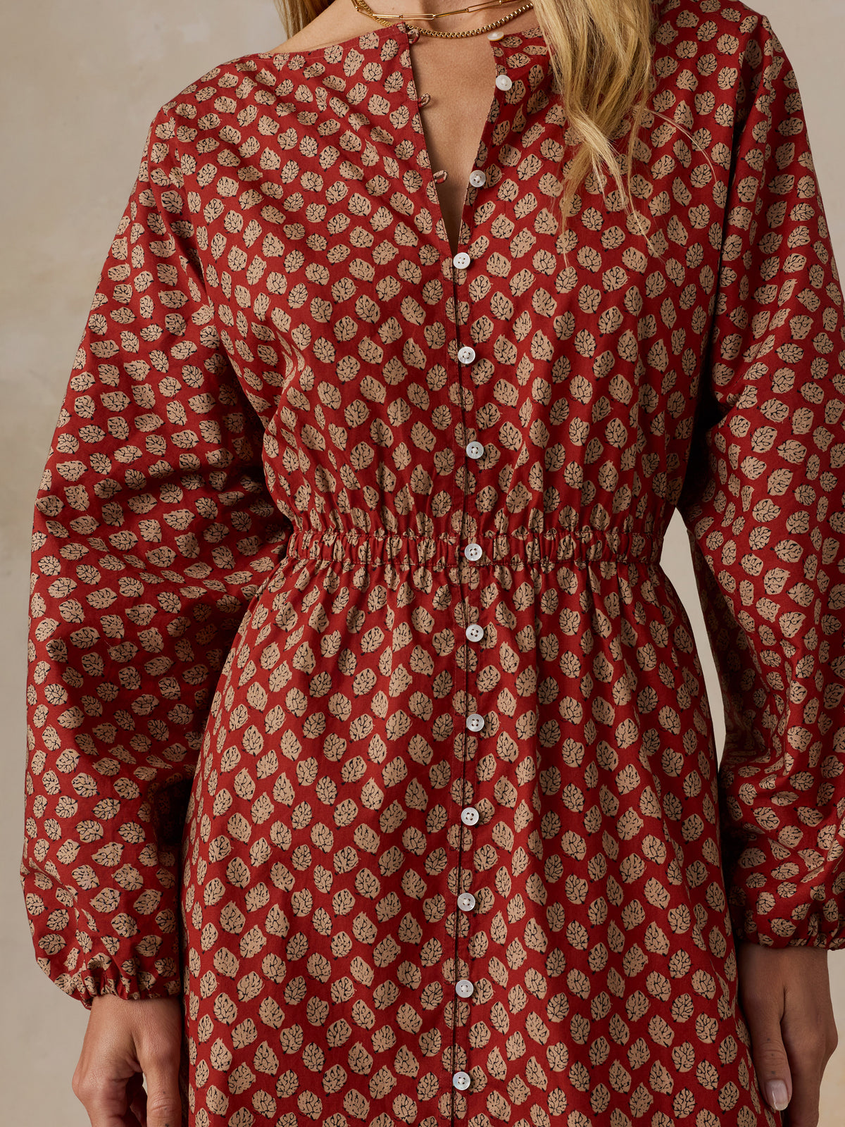 A close-up of a woman wearing a long-sleeve button-front dress with a gathered waist and an allover small floral print in rust red and beige., image 4 of 6