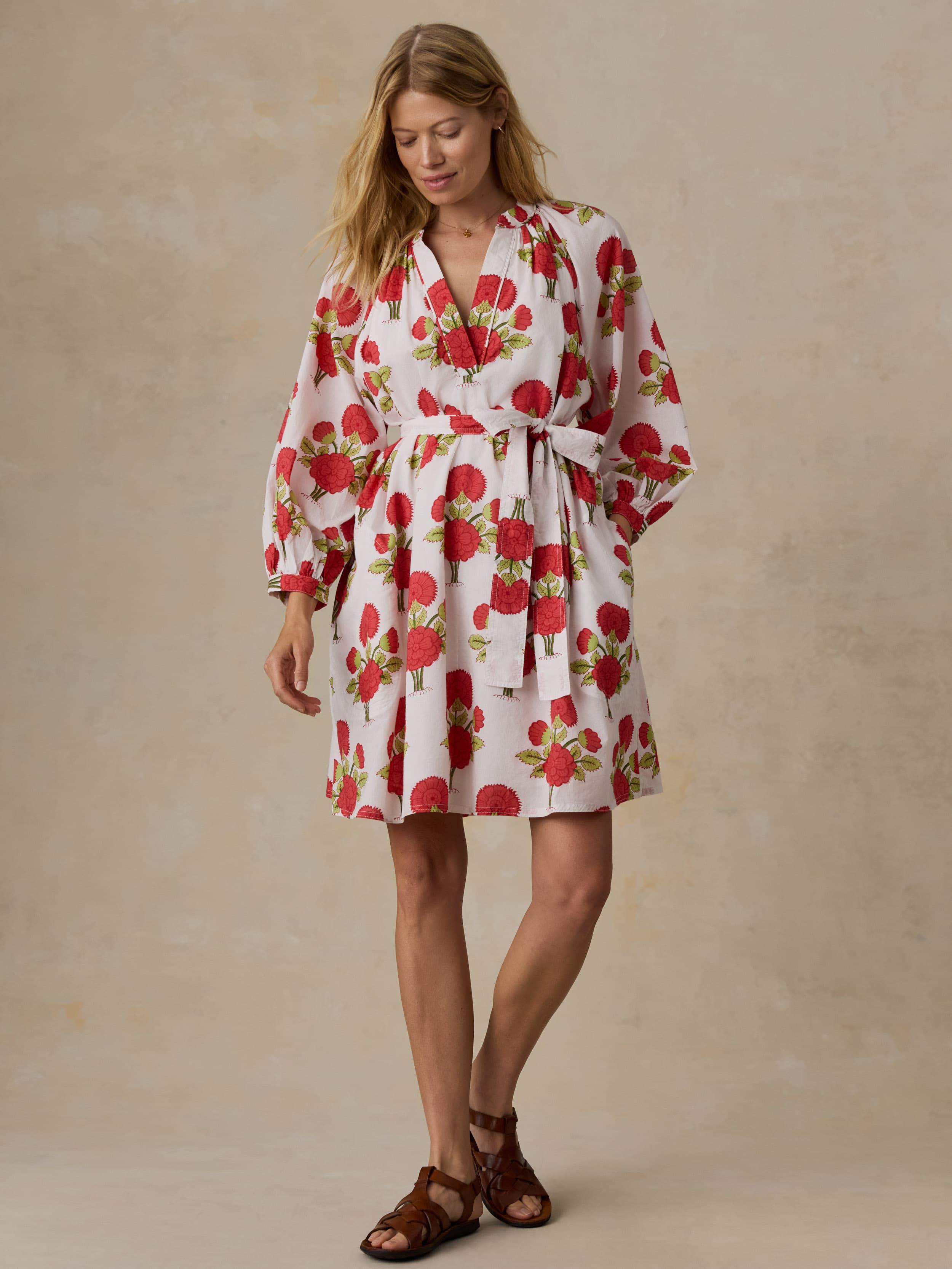 Woman wearing a white dress with red floral patterns on a beige background