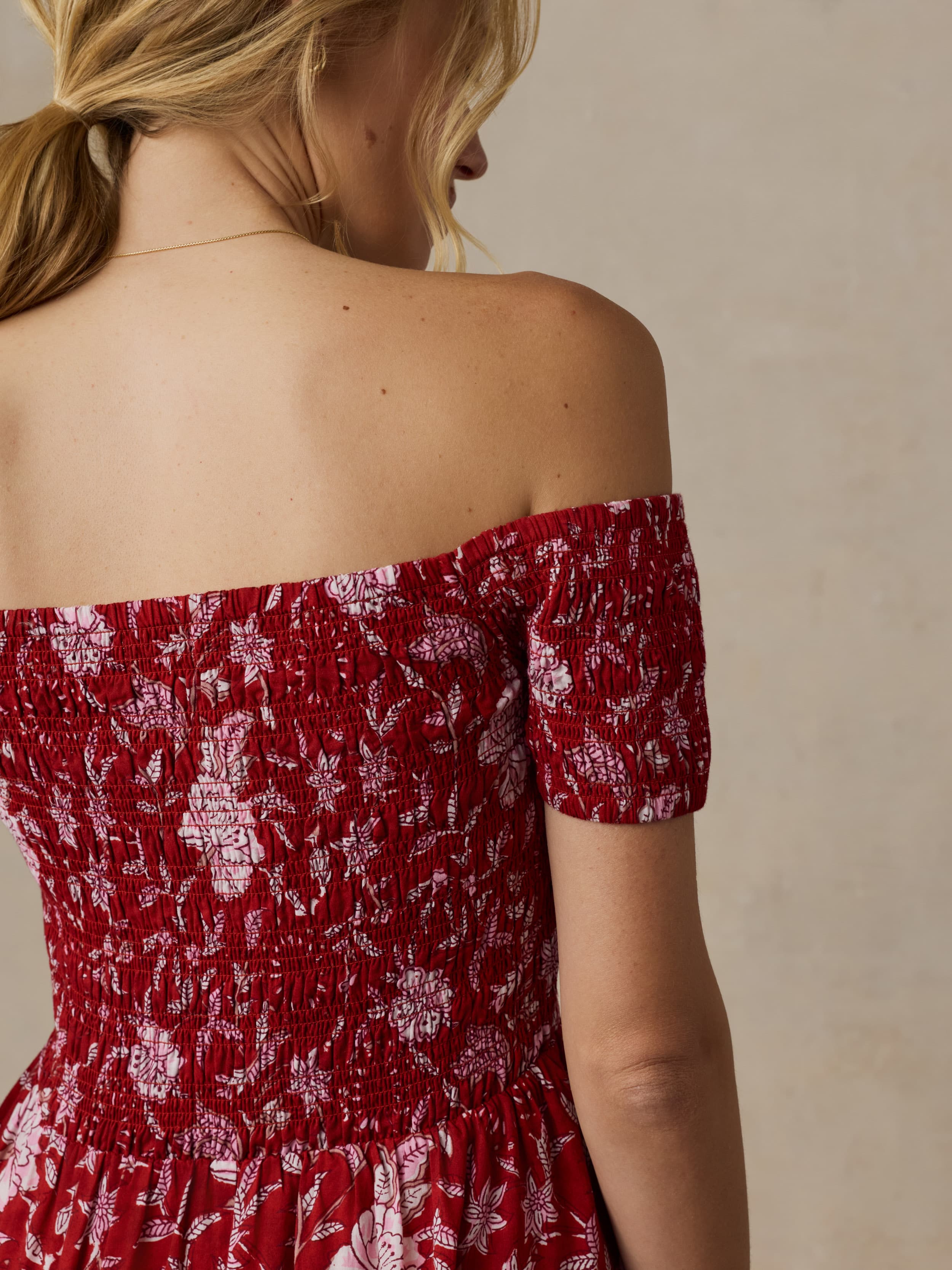 Woman wearing a red floral off-shoulder dress against a beige background