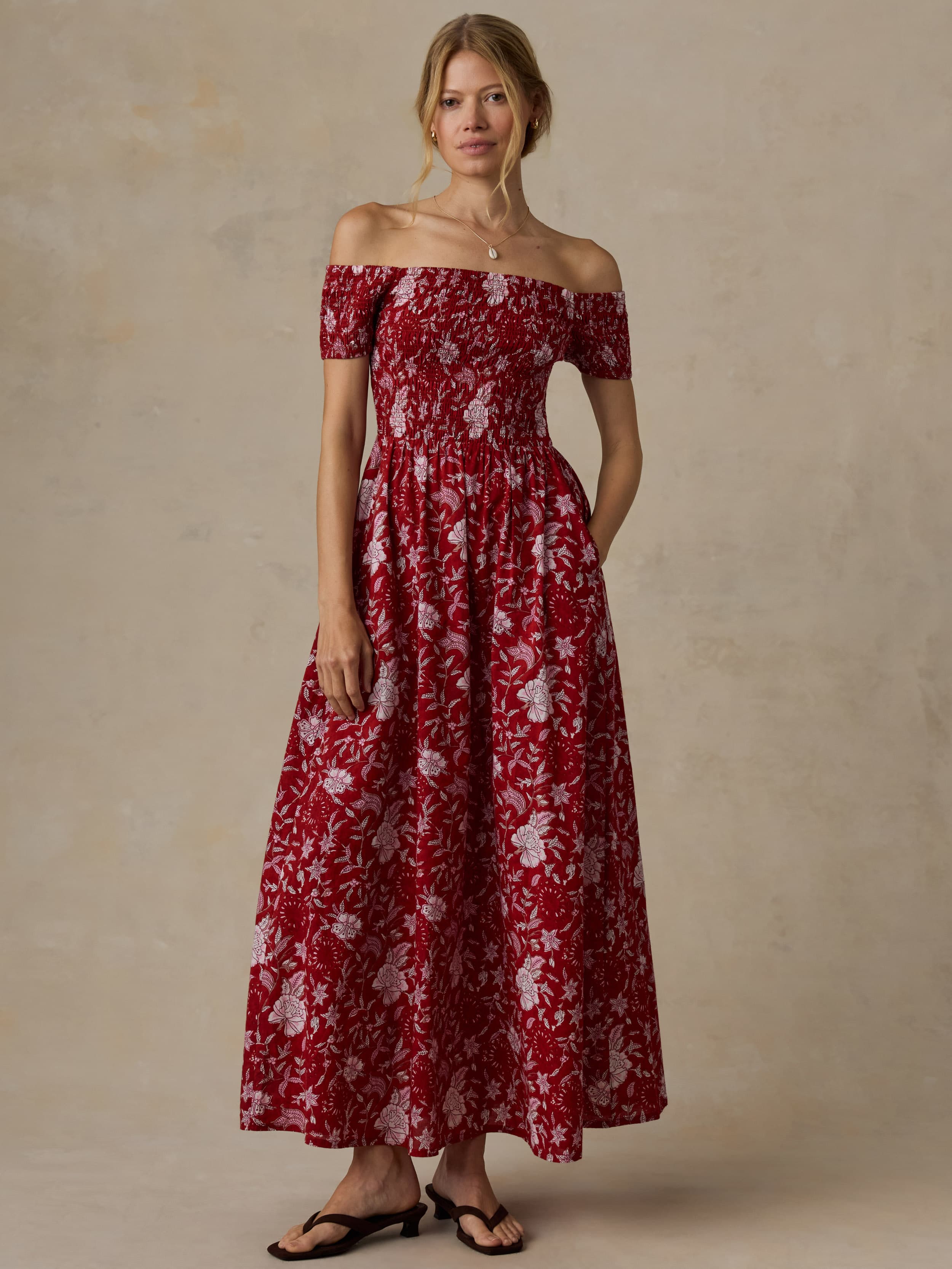 Woman wearing a red floral off-shoulder dress against a beige background