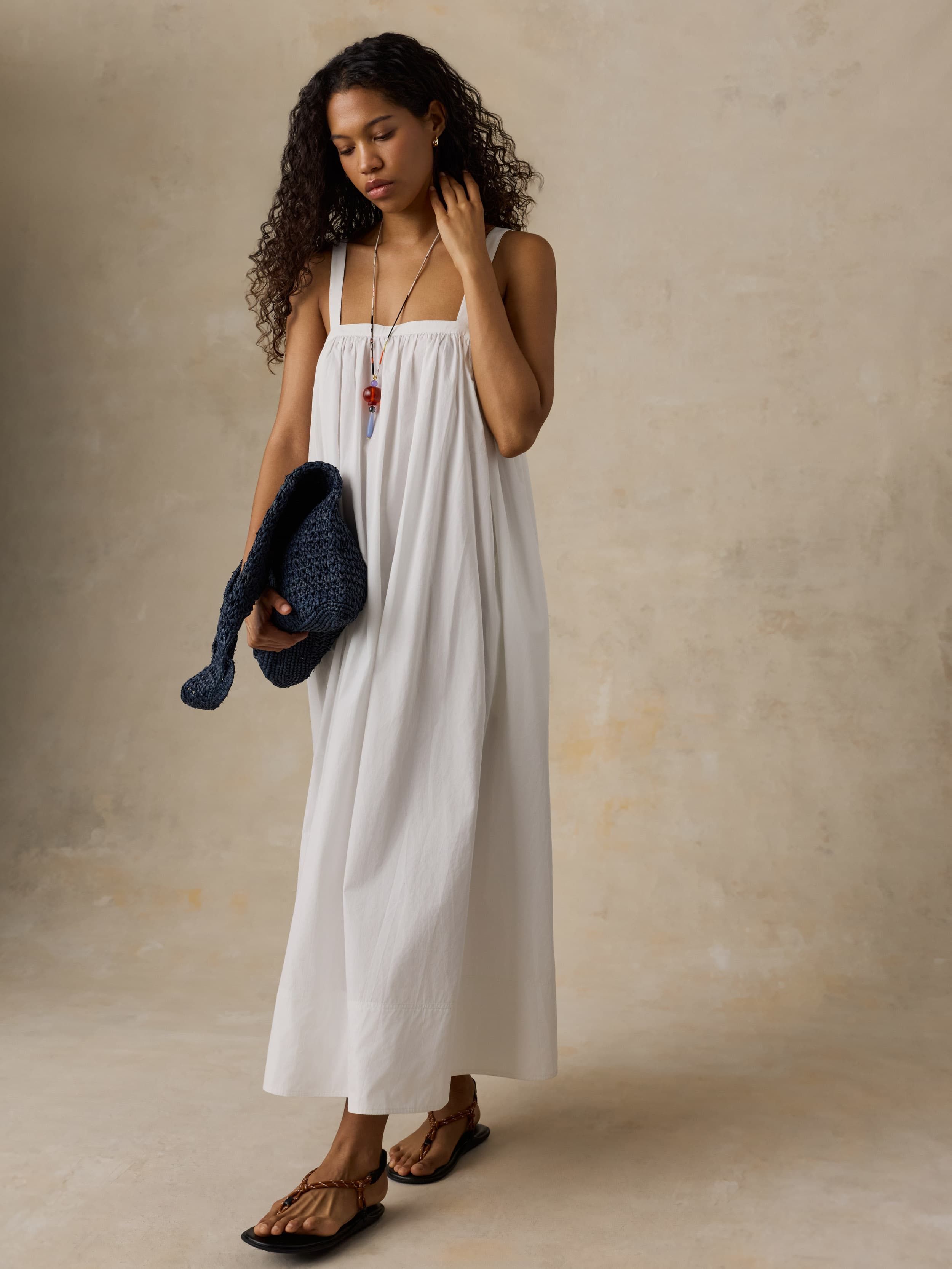 Woman in a white dress holding a blue bag against a beige background