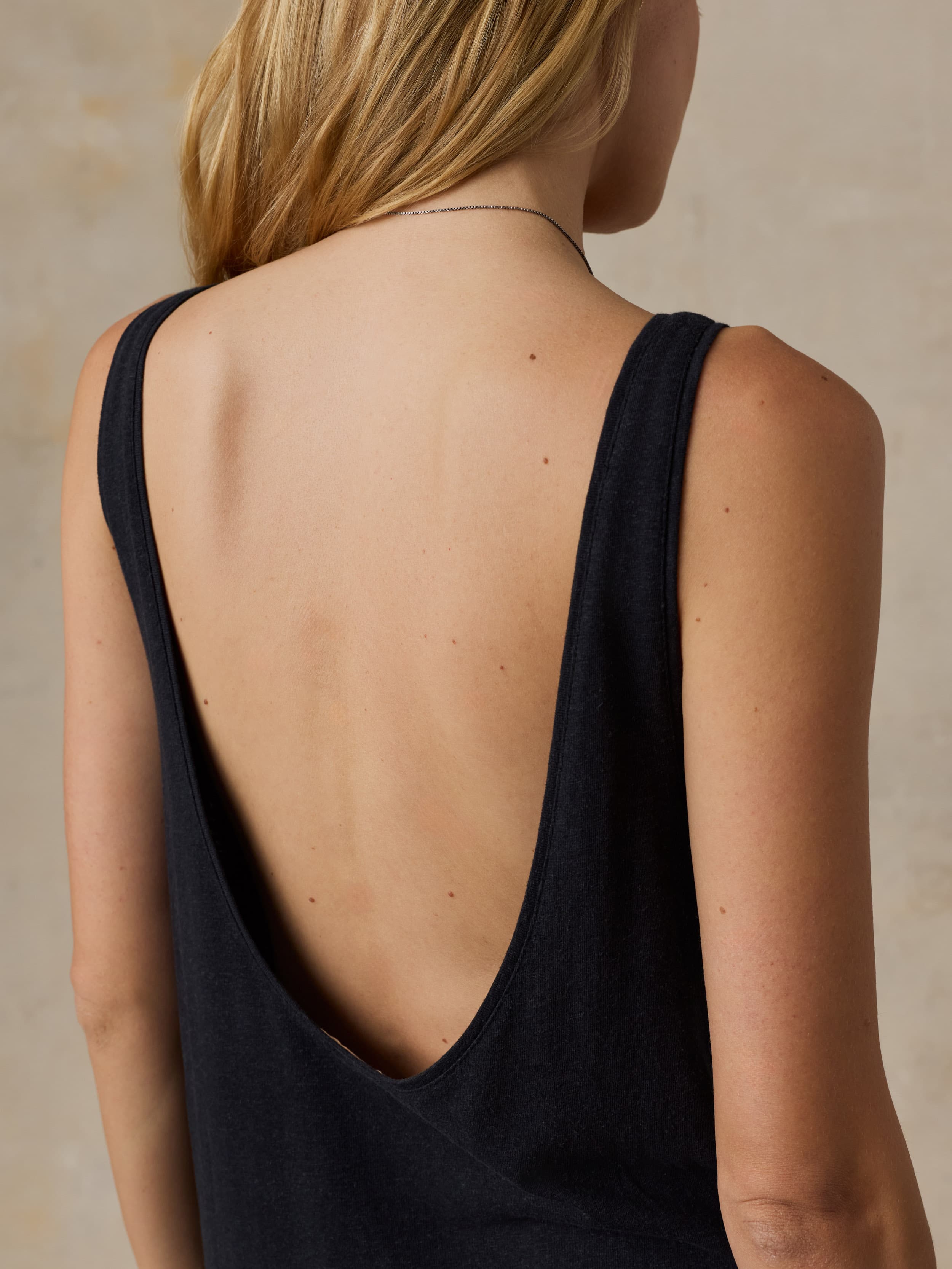 Woman wearing a black sleeveless dress against a beige background