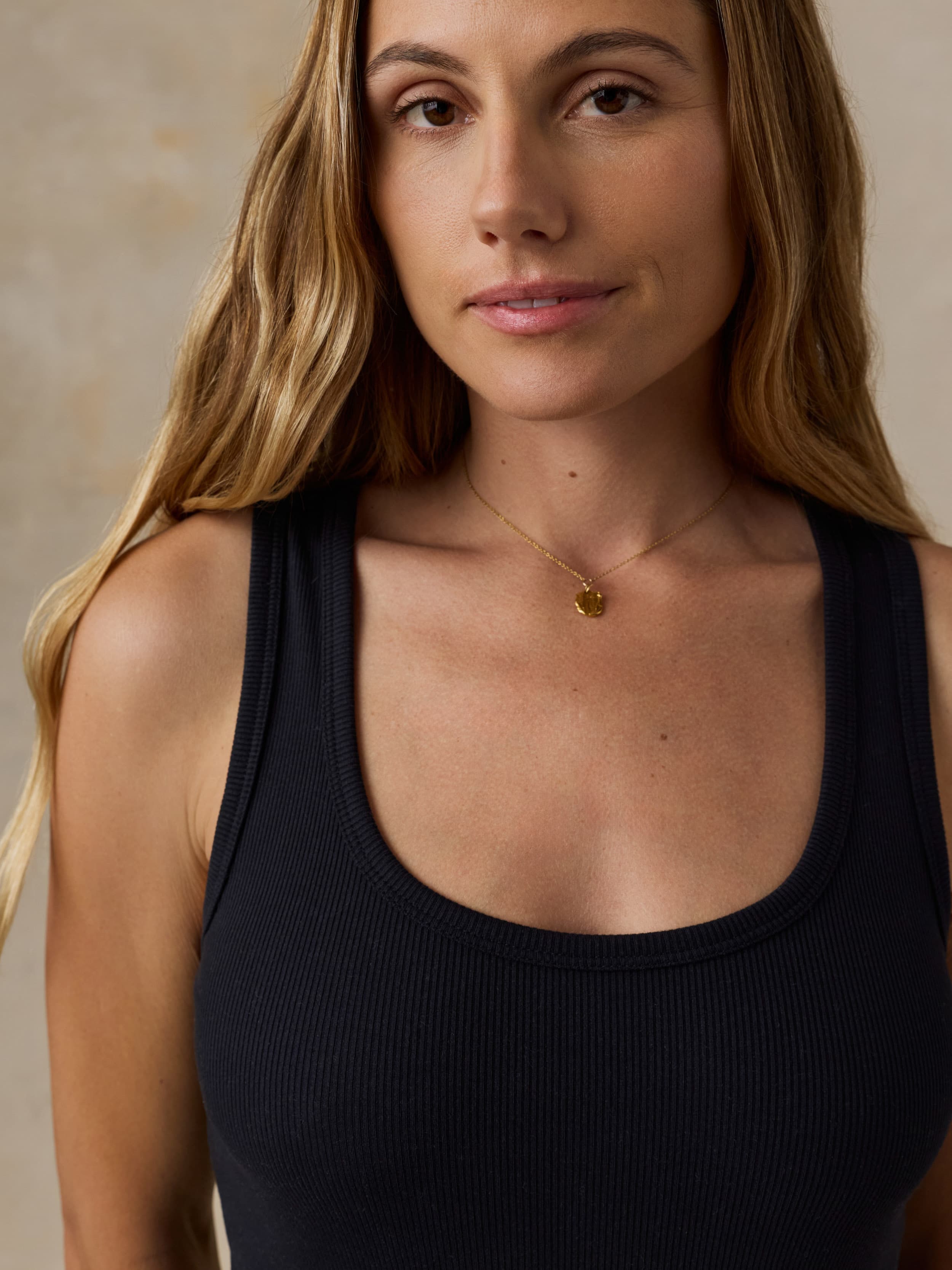 Woman wearing a black tank top and gold necklace against a neutral background