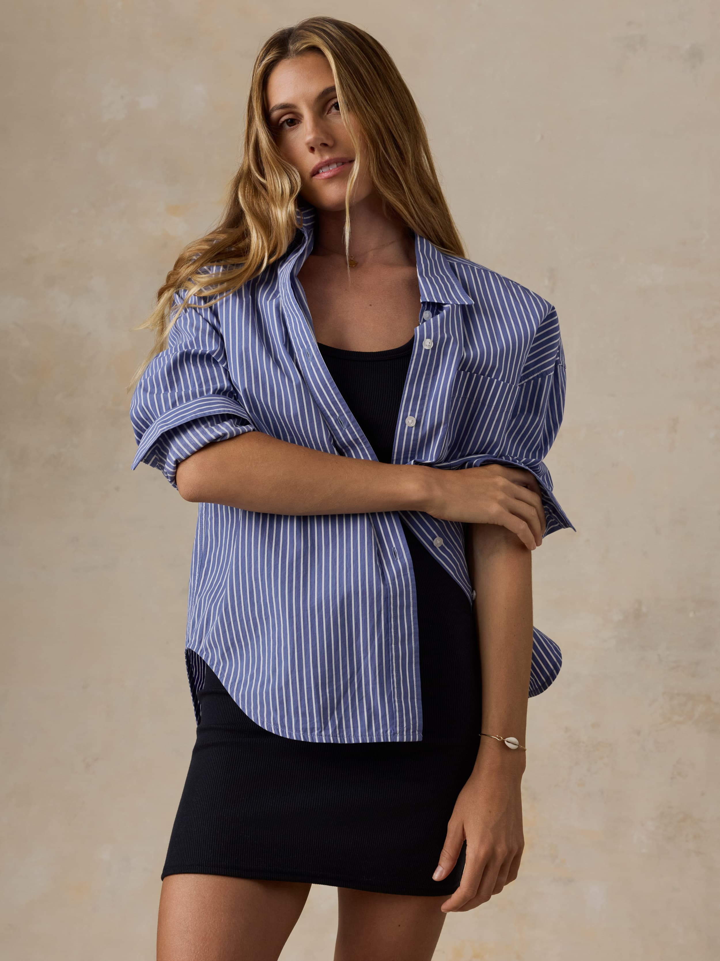 Woman wearing a blue striped shirt over a black dress and skirt on a beige background