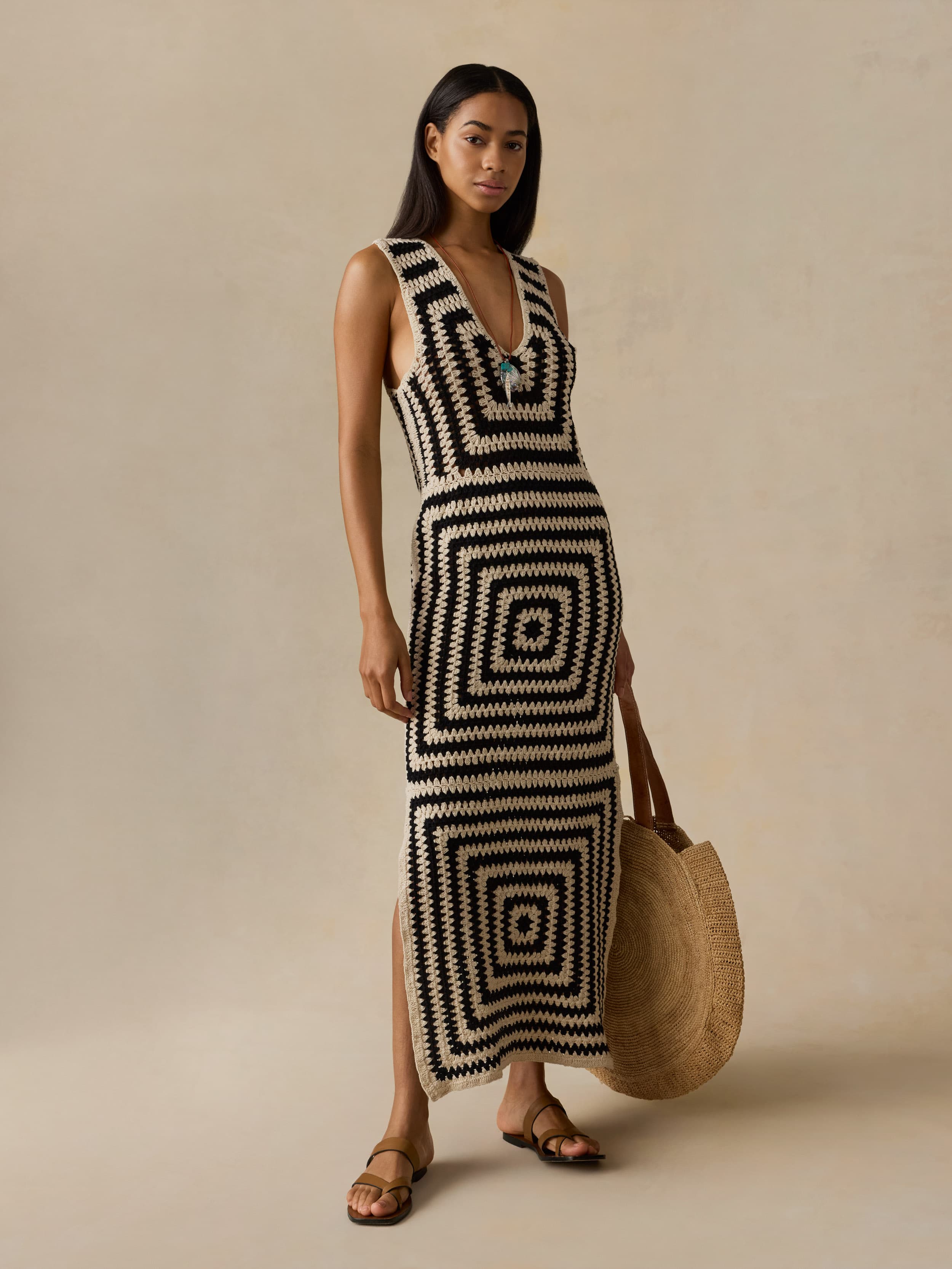 Woman wearing a black and white patterned dress holding a woven bag against a beige background
