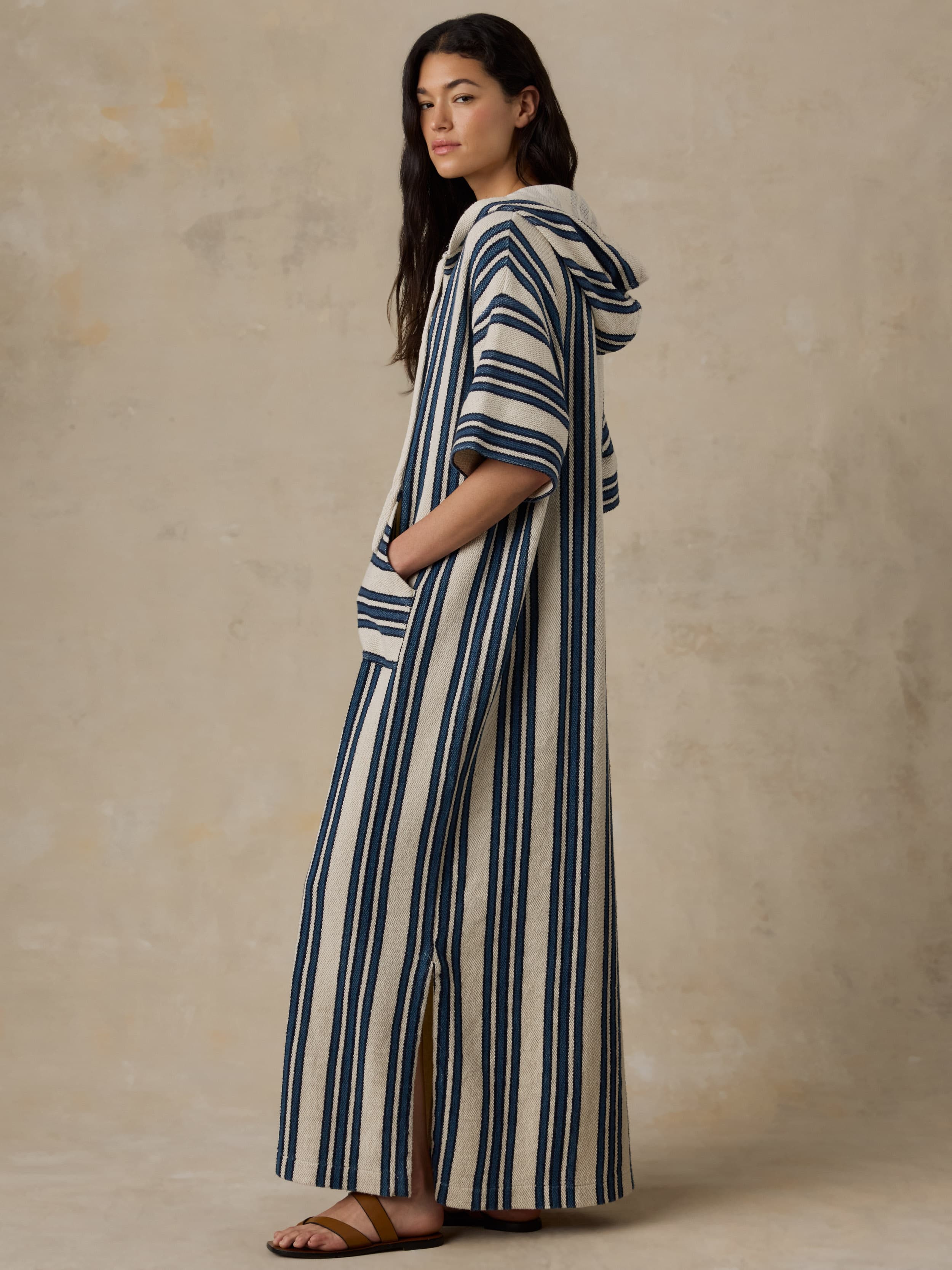 Woman wearing a long blue and white striped dress with a hood against a beige background