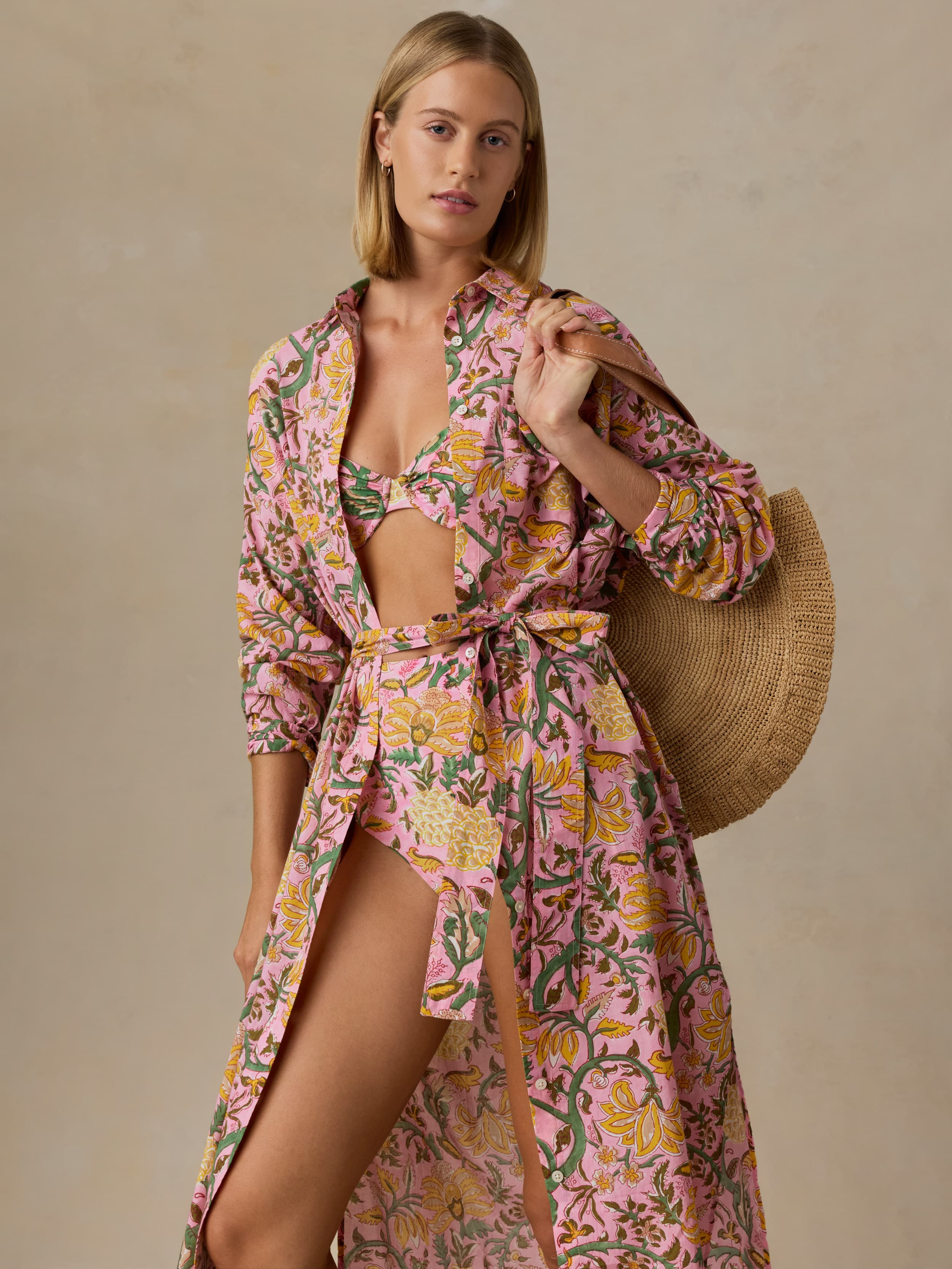 Woman wearing a floral dress with a straw bag on a beige background